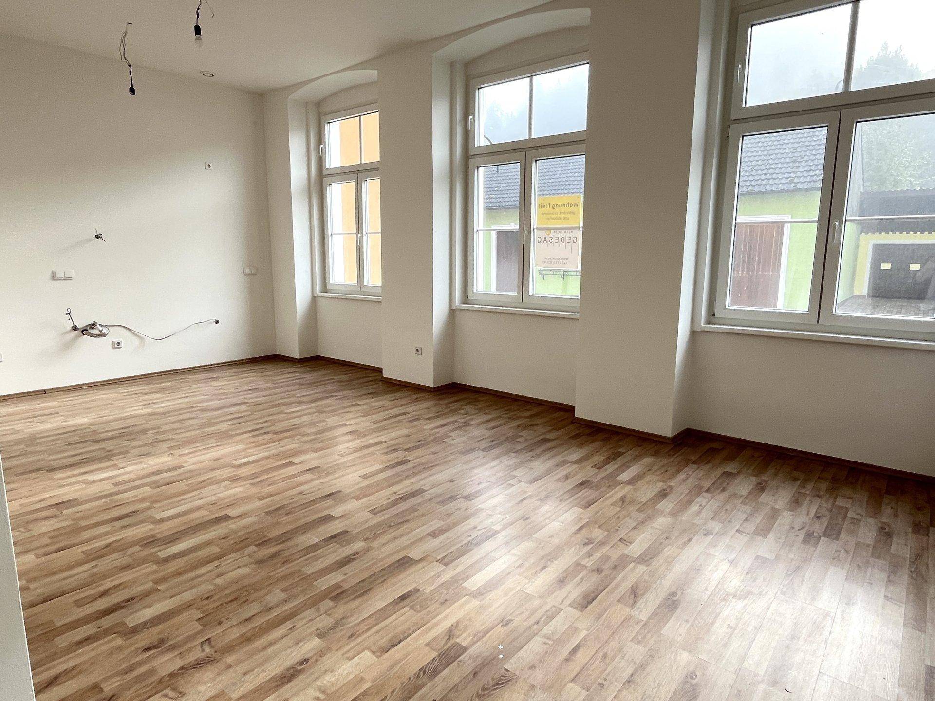 Großzügiger Wohnbereich mit mehreren Fenstern, Laminatboden und viel natürlichem Licht.