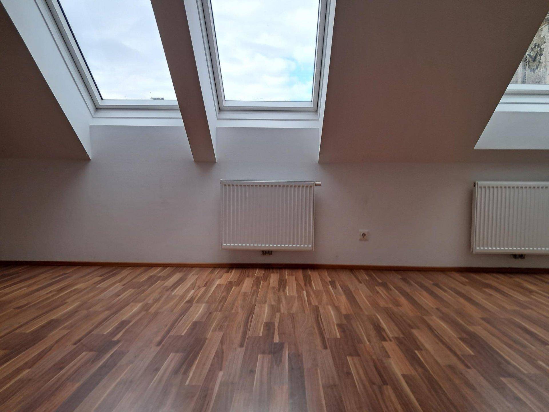 Heller Dachgeschossraum mit zwei großen Dachfenstern und Laminatboden, gut beleuchtet.