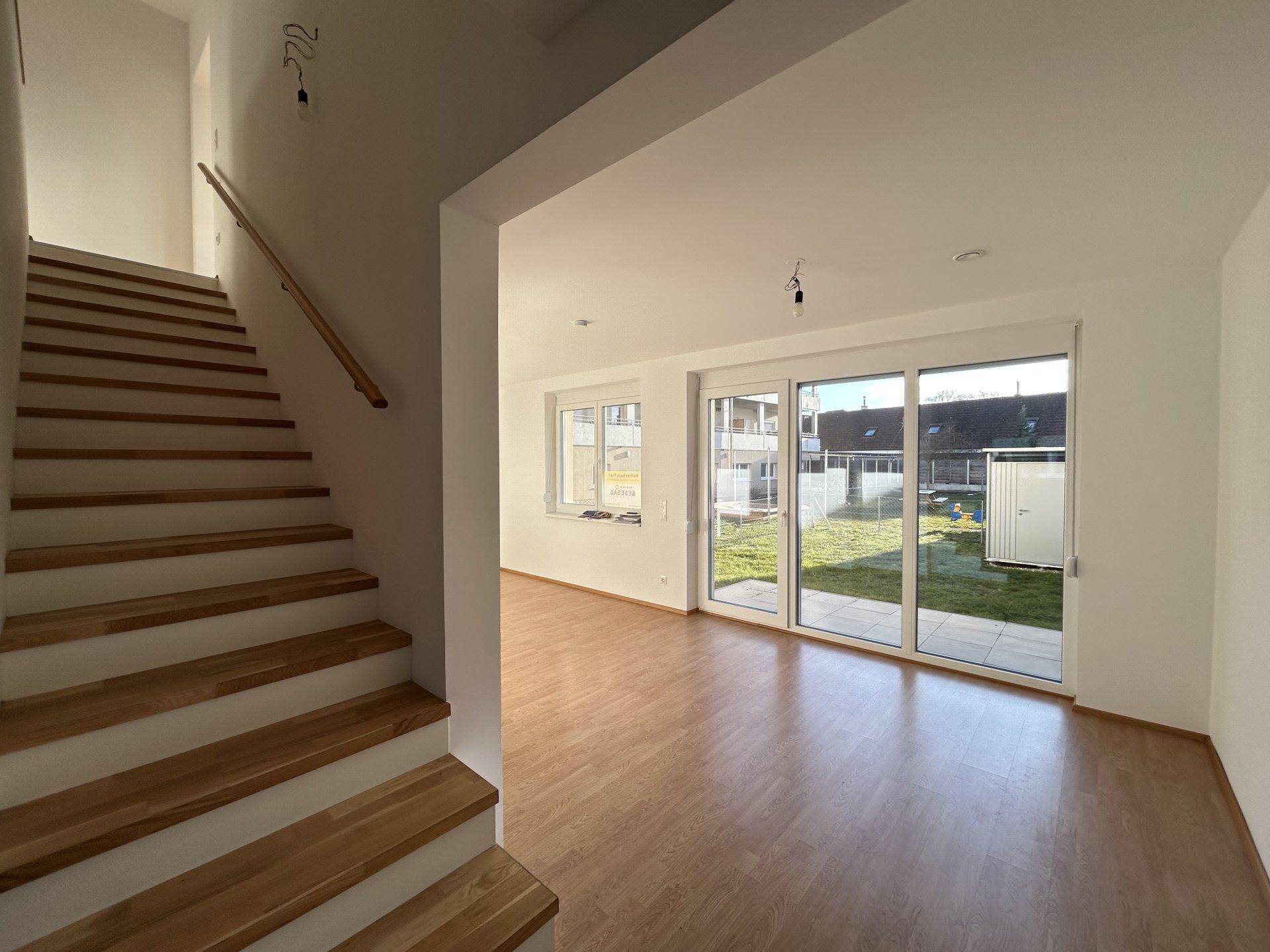 Heller Wohnbereich mit Holztreppe und Blick auf den Garten durch große Schiebetüren.