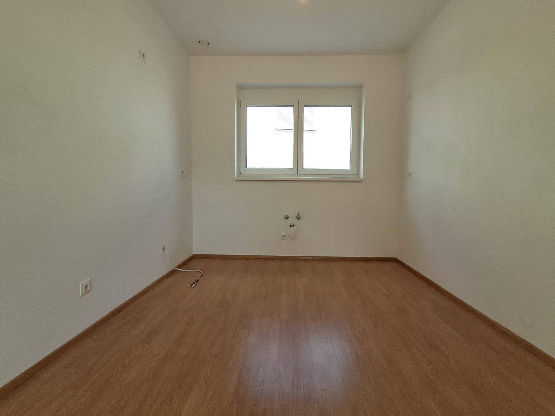 Kleiner Raum mit Laminatboden und Fenster, vorbereitet für Installationen, ideal als Hauswirtschaftsraum.