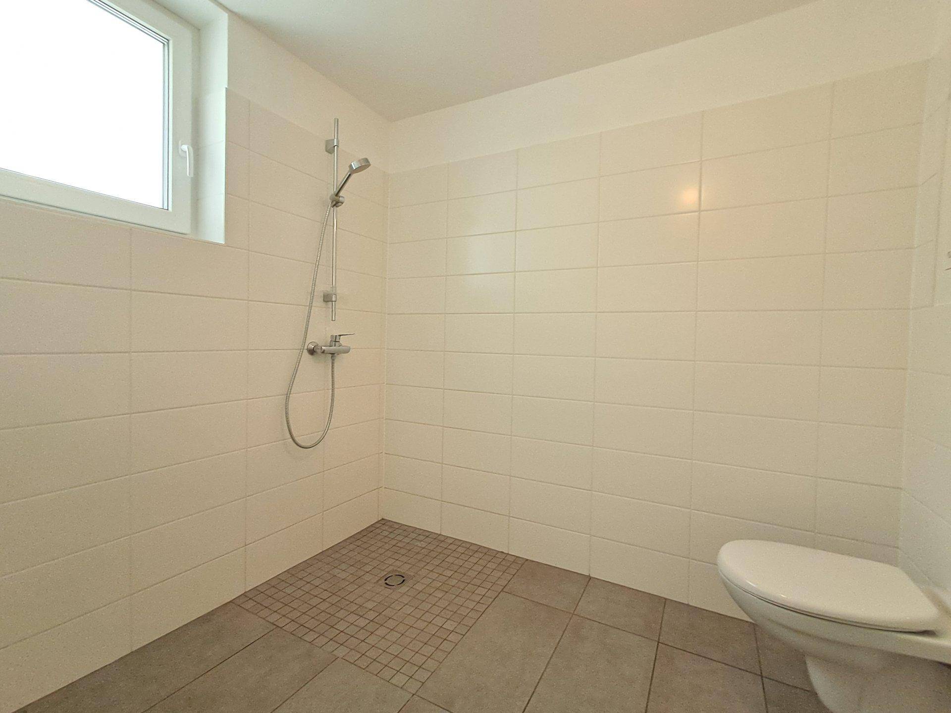 Modernes Badezimmer mit ebenerdiger Dusche, WC und hellen Fliesen an Wänden und Boden.