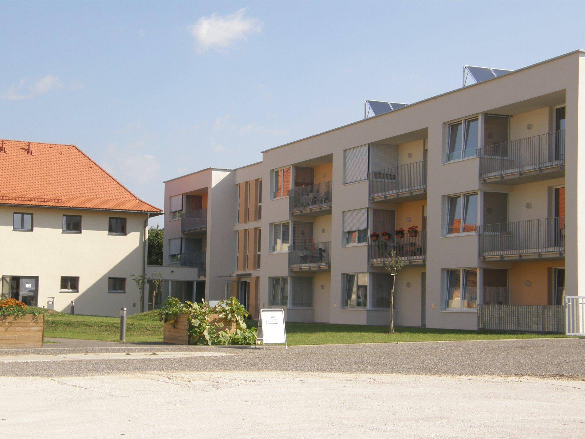 Moderne Wohngebäude mit Balkonen und Solaranlagen auf dem Dach, umgeben von Grünflächen.