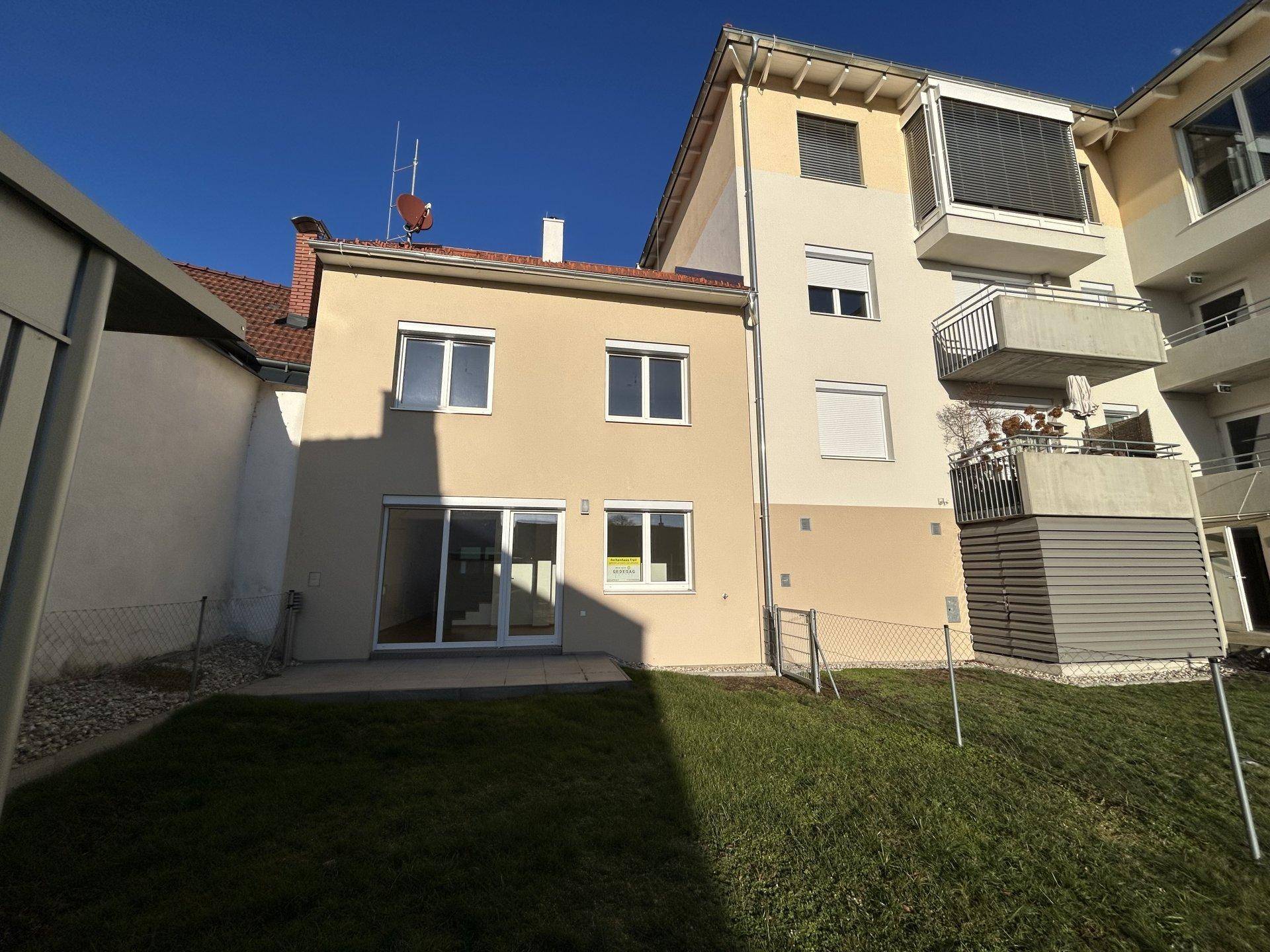 Rückseite des Hauses mit Terrasse und Garten, umgeben von anderen Gebäuden.