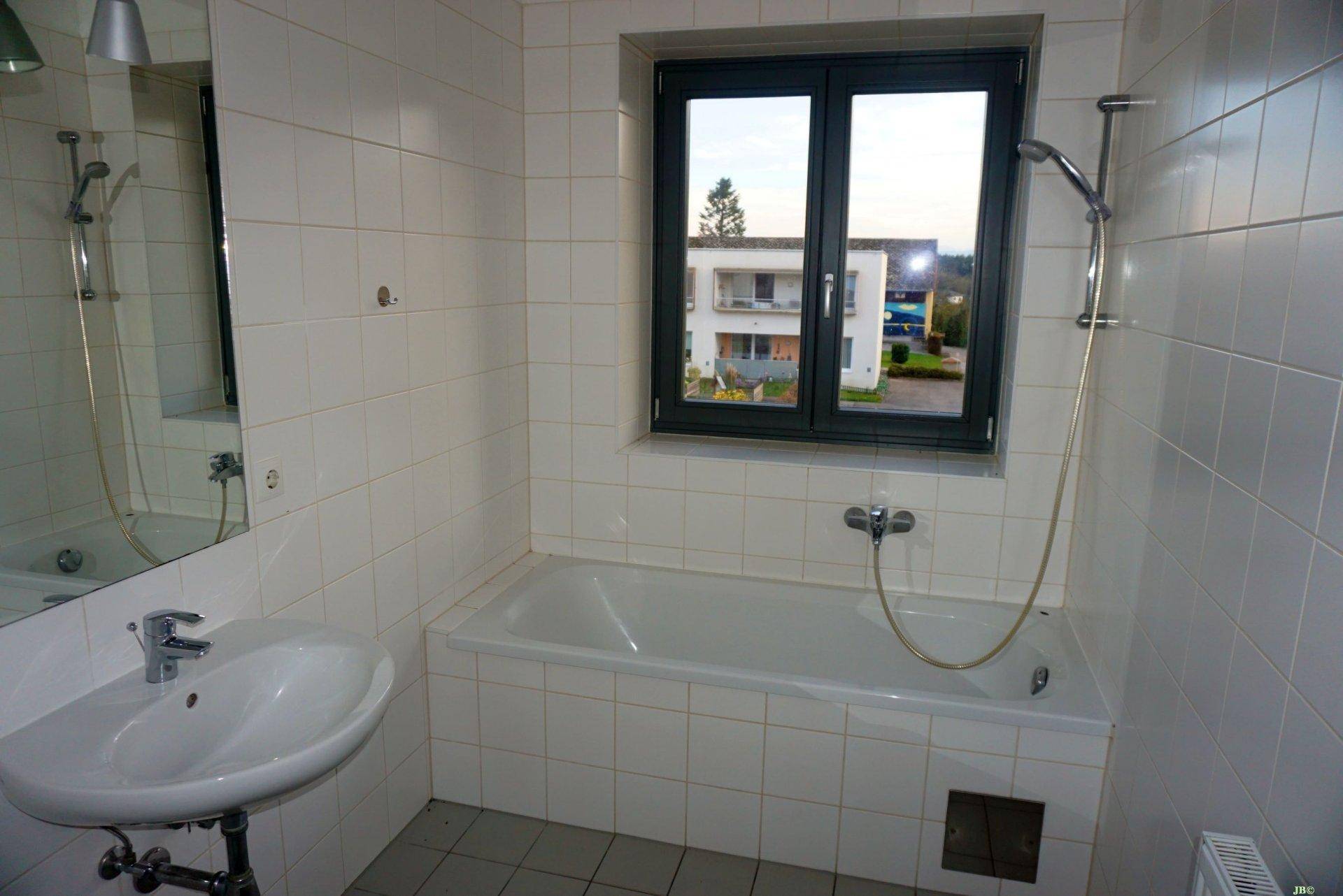 Gefliestes Badezimmer mit Badewanne, Waschbecken und Fenster.