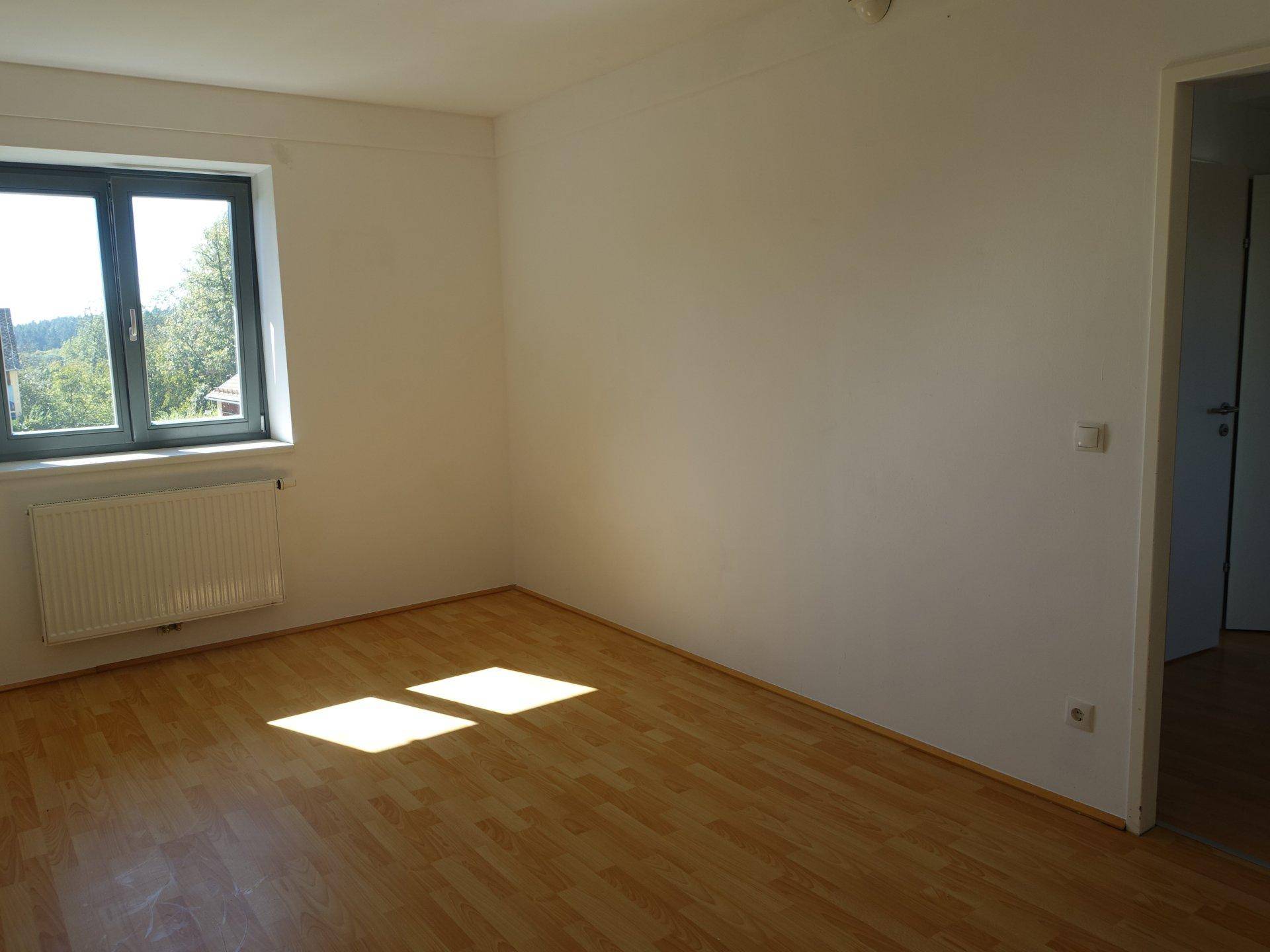 Helles Zimmer mit Laminatboden und Fenster, das viel Sonnenlicht hereinlässt.