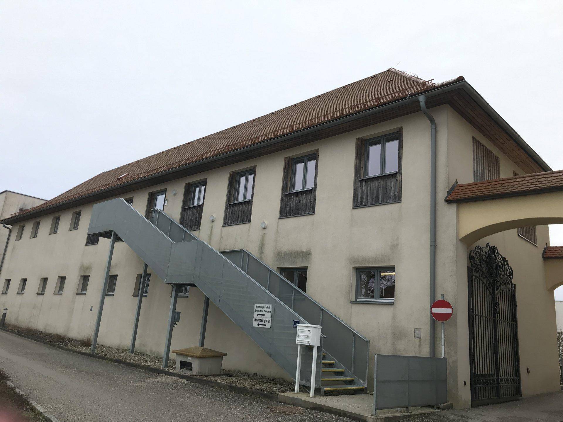 Seitenansicht eines Gebäudes mit externer Treppe und traditionellem Ziegeldach unter bewölktem Himmel.