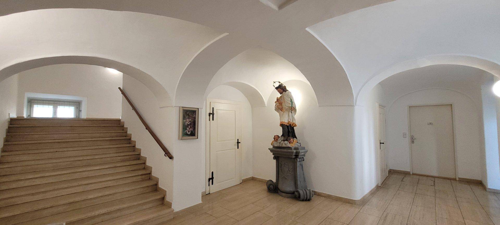Geräumiger Flur mit historischen Gewölben und einem dekorativen Standbild in einem Altbau.