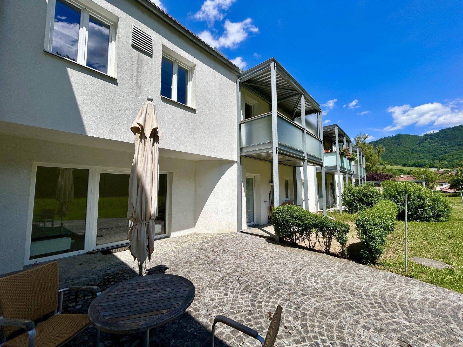 Gepflasterte Terrasse mit Sonnenschirm und Sitzgelegenheiten vor der Gebäudefassade mit Balkonen.