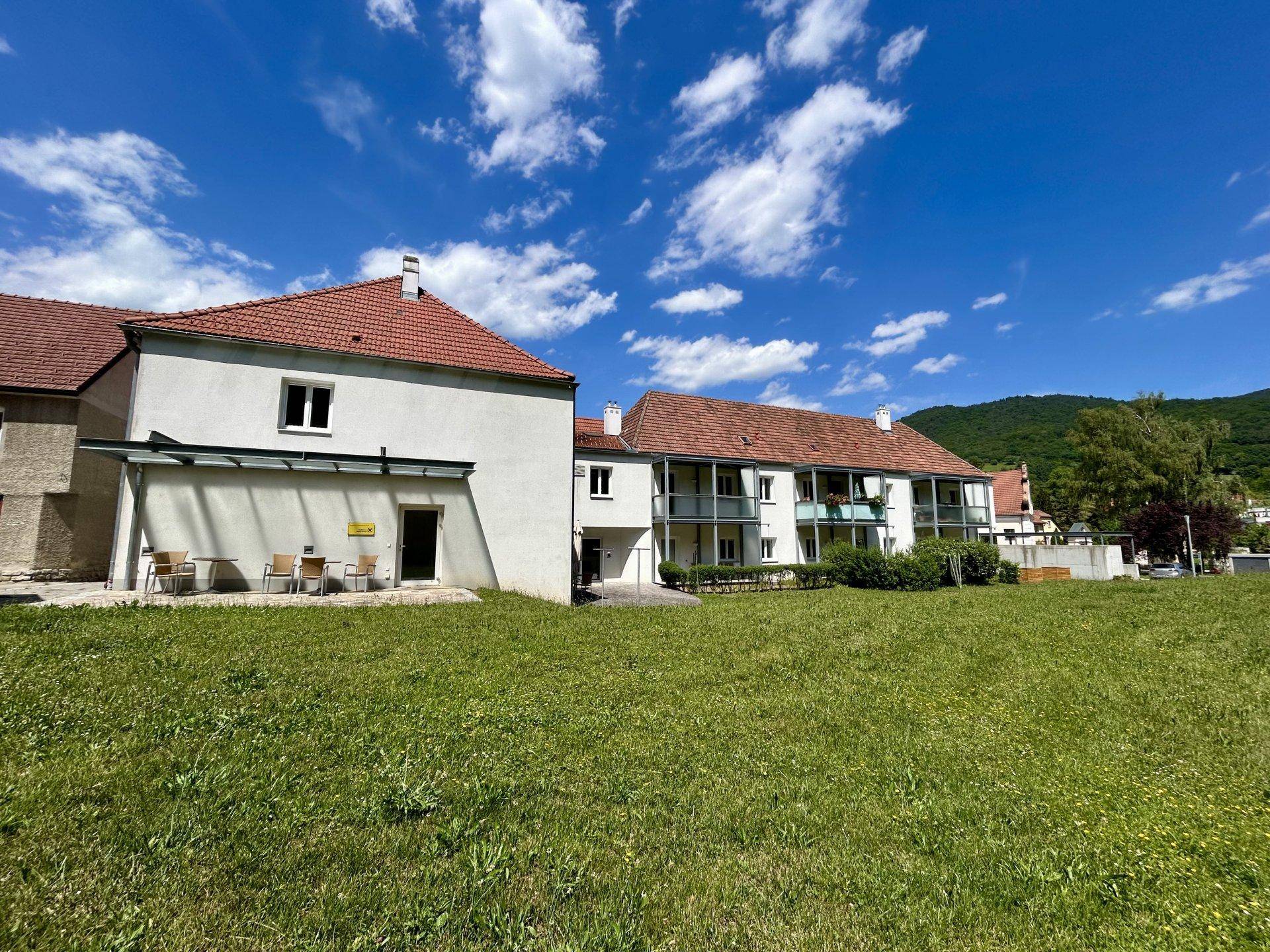 Ansicht des Wohngebäudes mit großem Rasenbereich und angrenzender grüner Hügellandschaft.