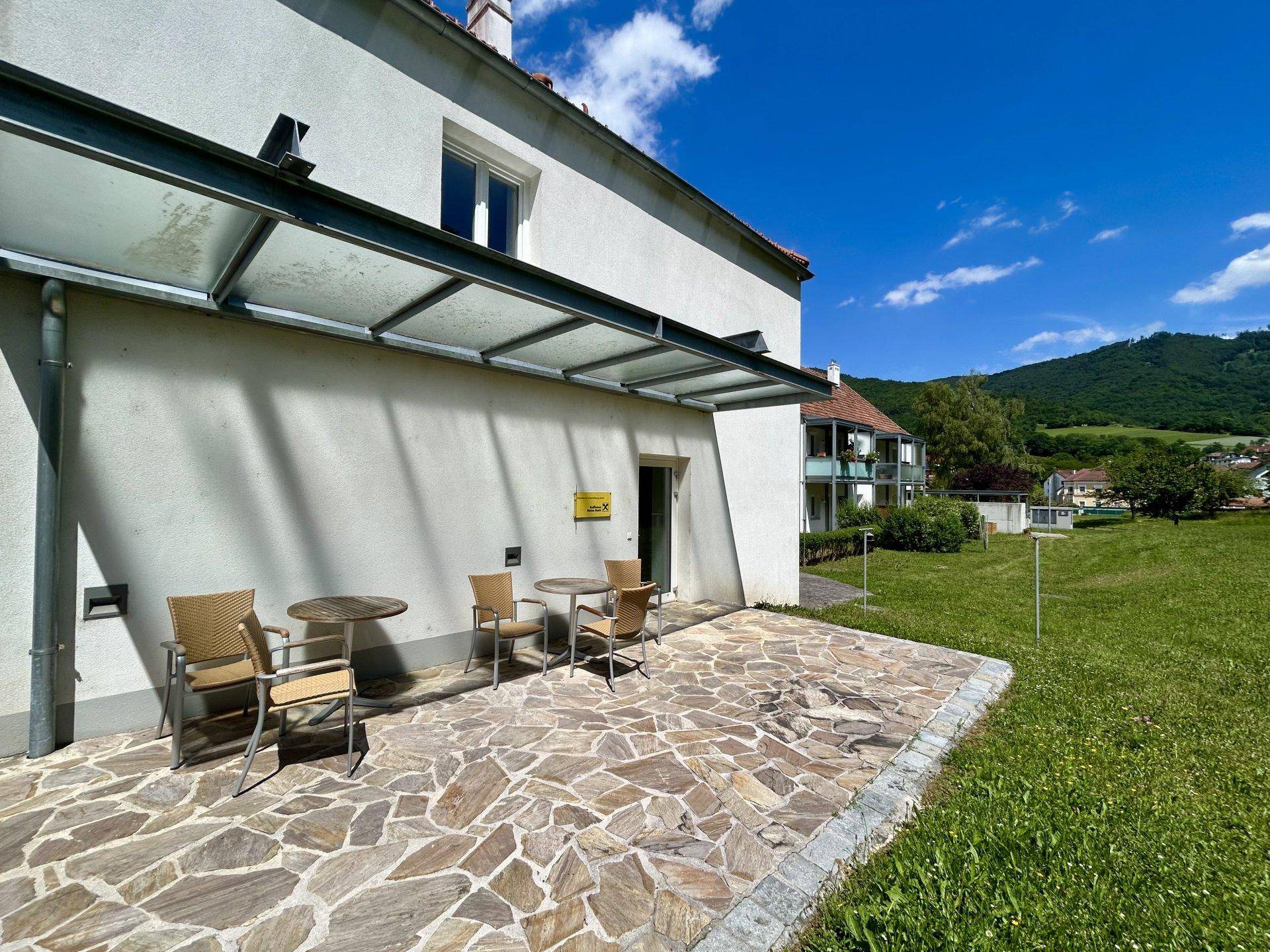 Überdachte Terrasse mit Steinfliesen und Gartenmöbeln, umgeben von grüner Landschaft.