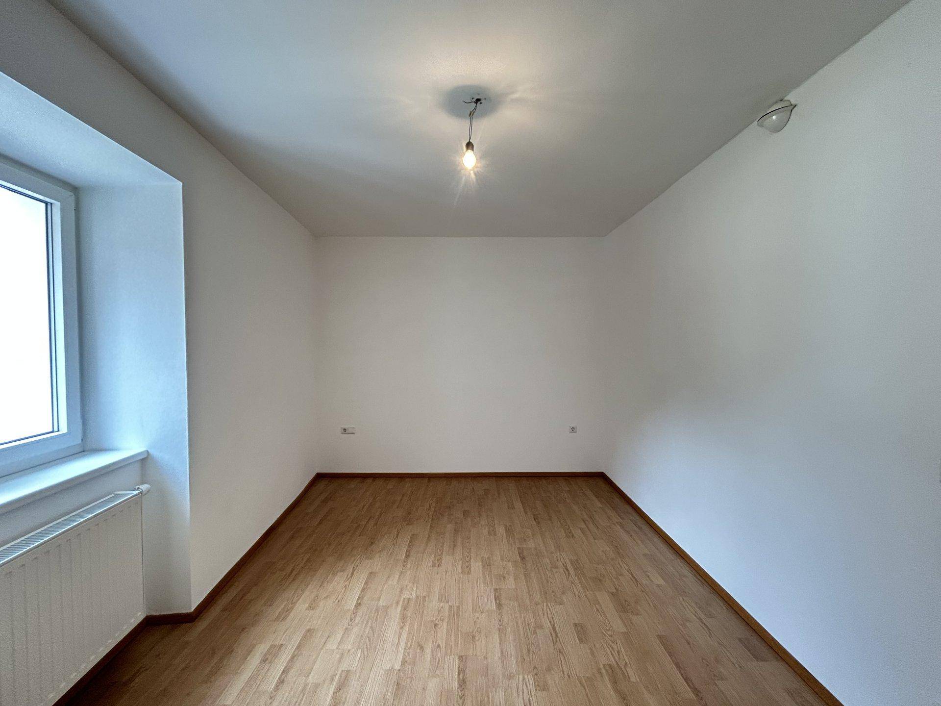 Leeres Schlafzimmer mit hellem Holzfußboden und großem Fenster, bereit zur Einrichtung.