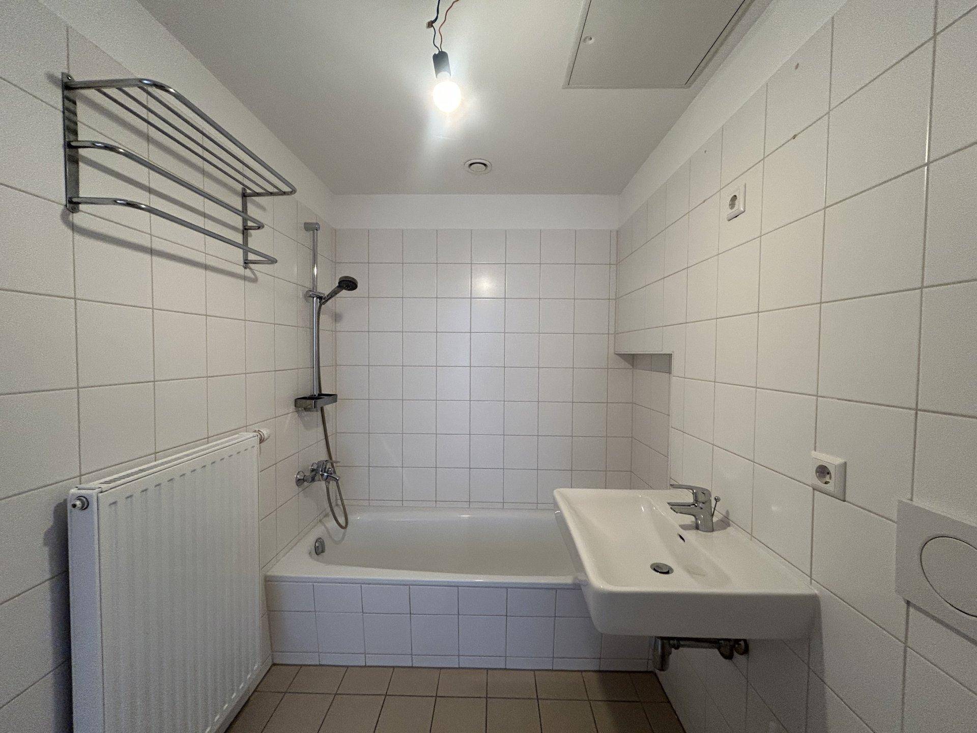 Funktionales Badezimmer mit Badewanne, Waschbecken und weißen Fliesen an Wänden und Boden.