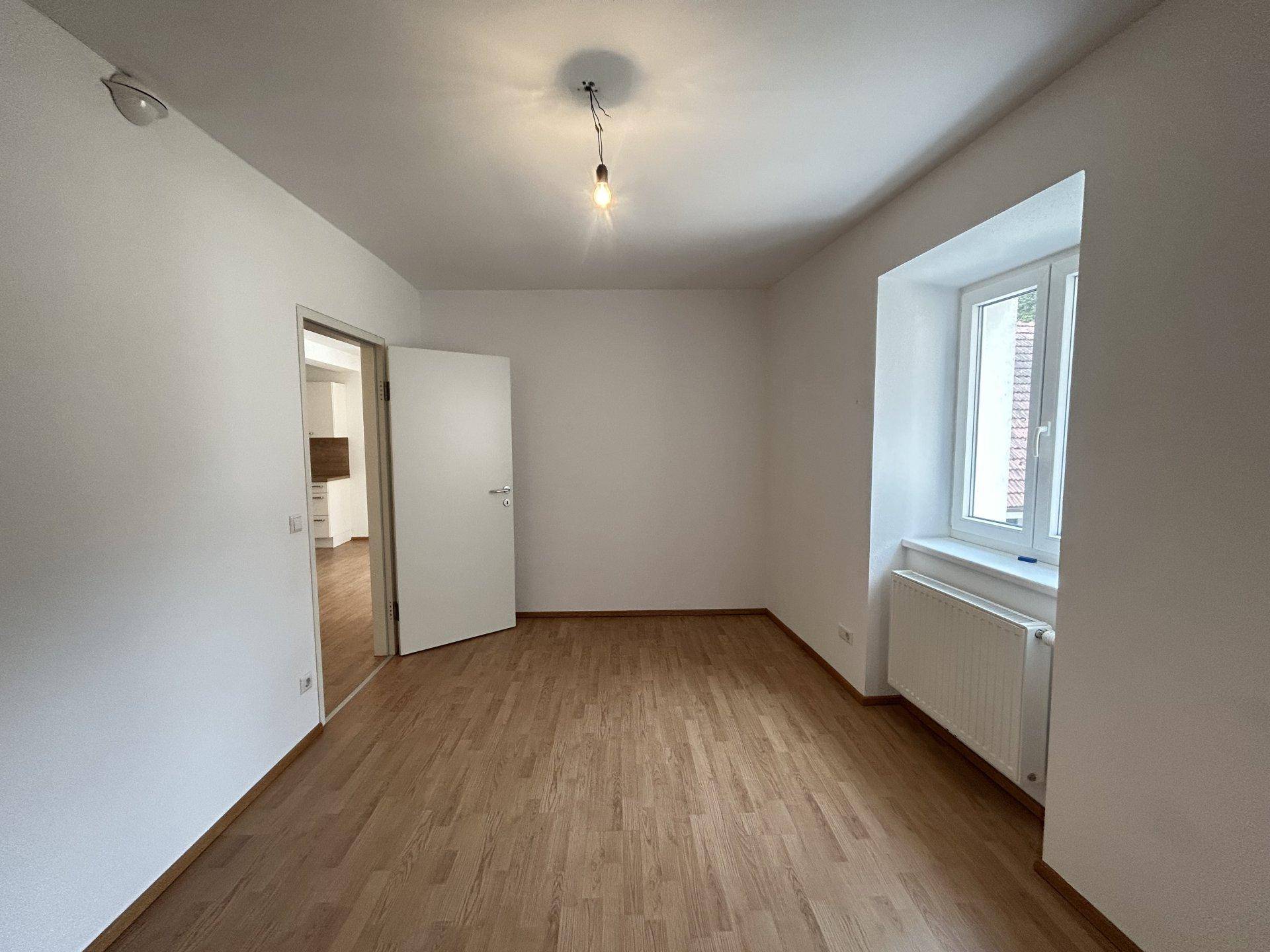 Helles Schlafzimmer mit Holzboden und Fenster, das einen Blick nach draußen bietet.