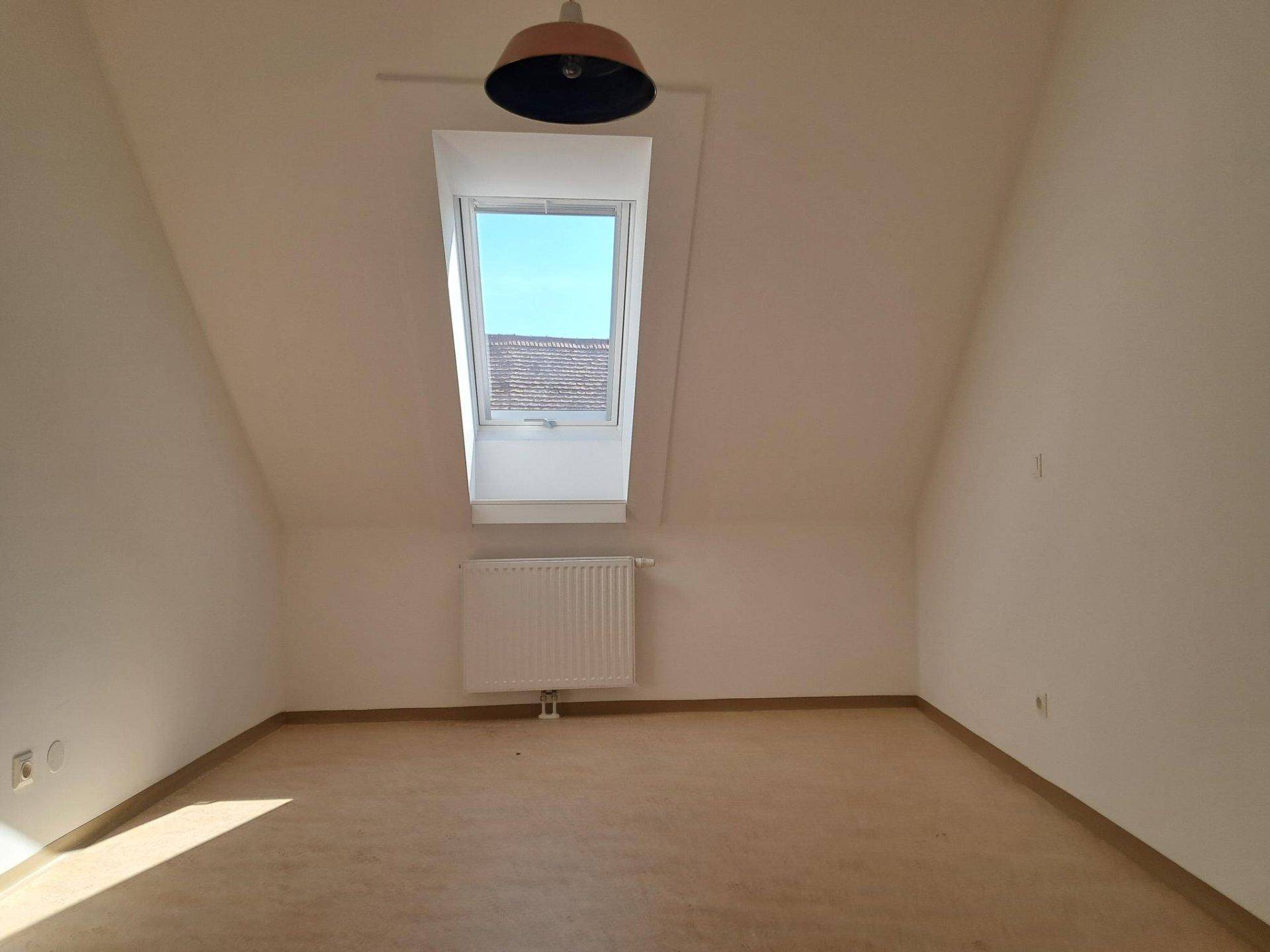 Gemütlicher Dachgeschossraum mit schrägen Wänden, einem Dachfenster und hellem Boden.