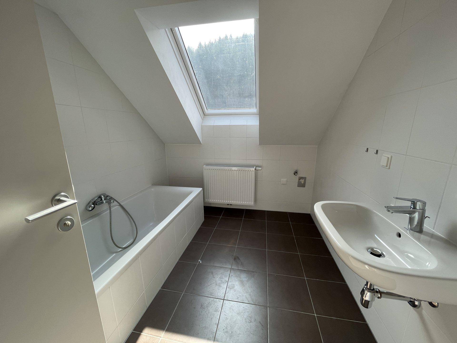 Badezimmer mit Badewanne, Waschbecken und Dachfenster unter einer Dachschräge.