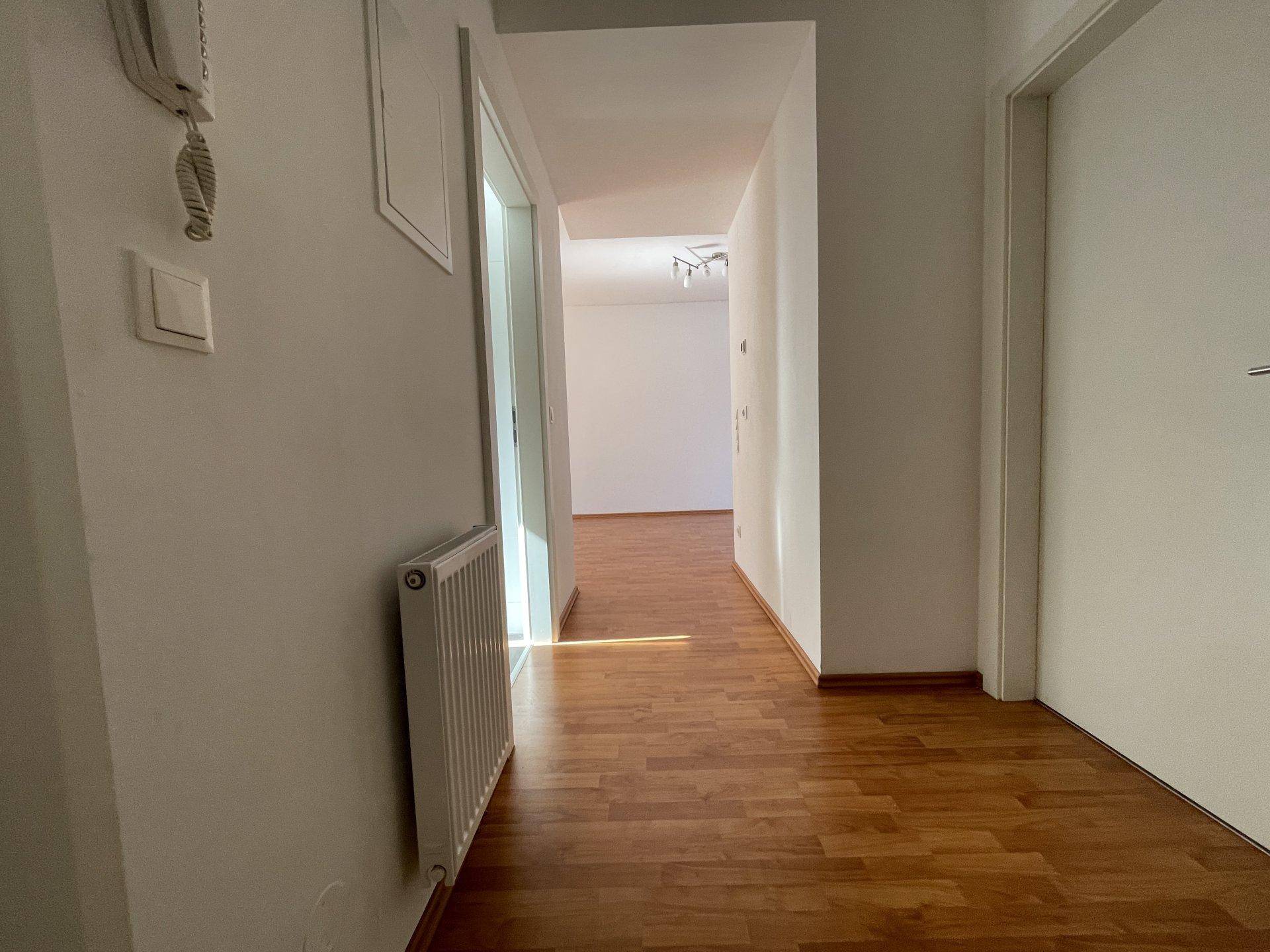 Heller Flur mit Holzfußboden und weiß gestrichenen Wänden, der zu weiteren Räumen führt.
