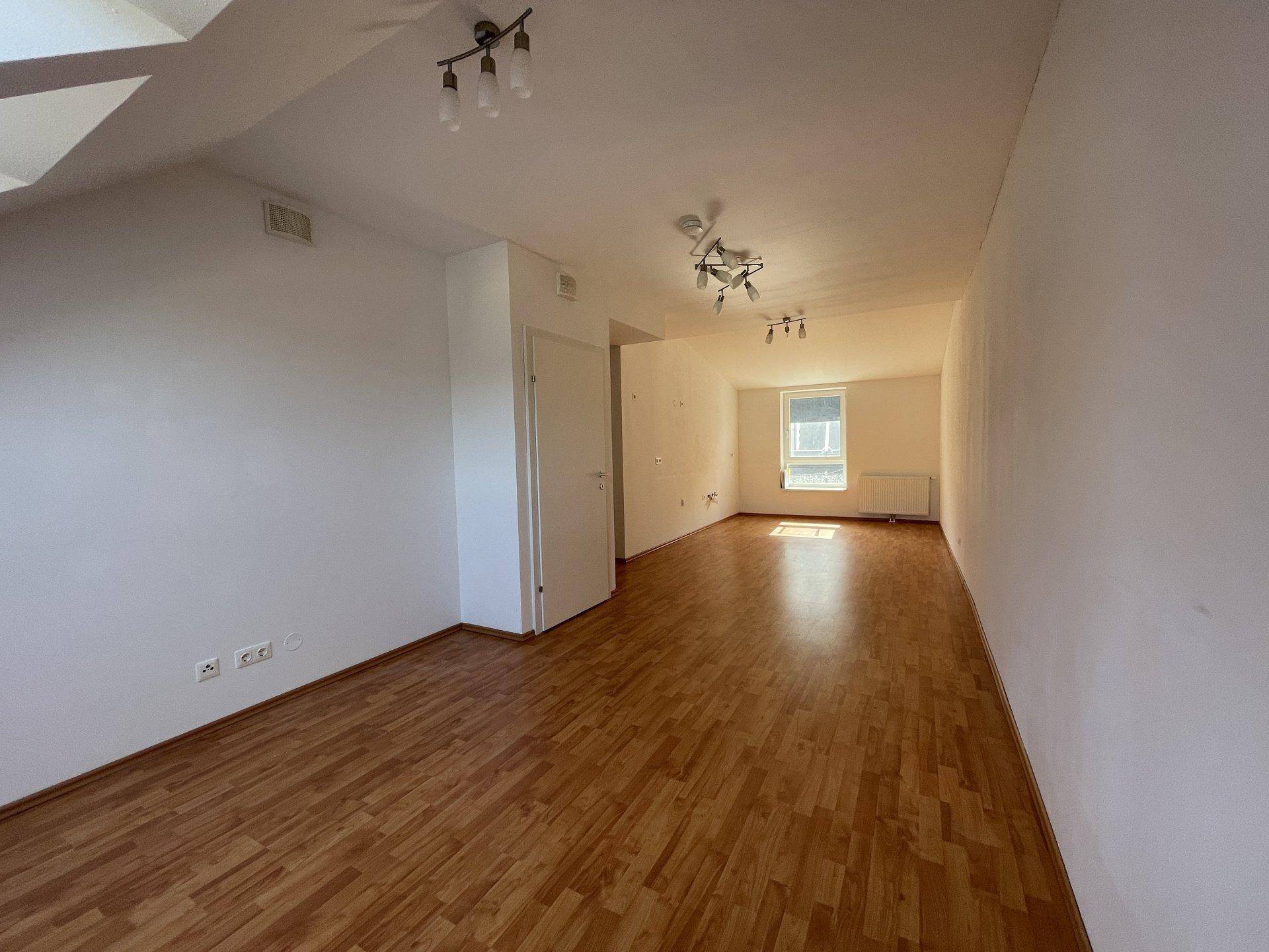 Geräumiger leerer Raum im Dachgeschoss mit Holzfußboden und einem Fenster.