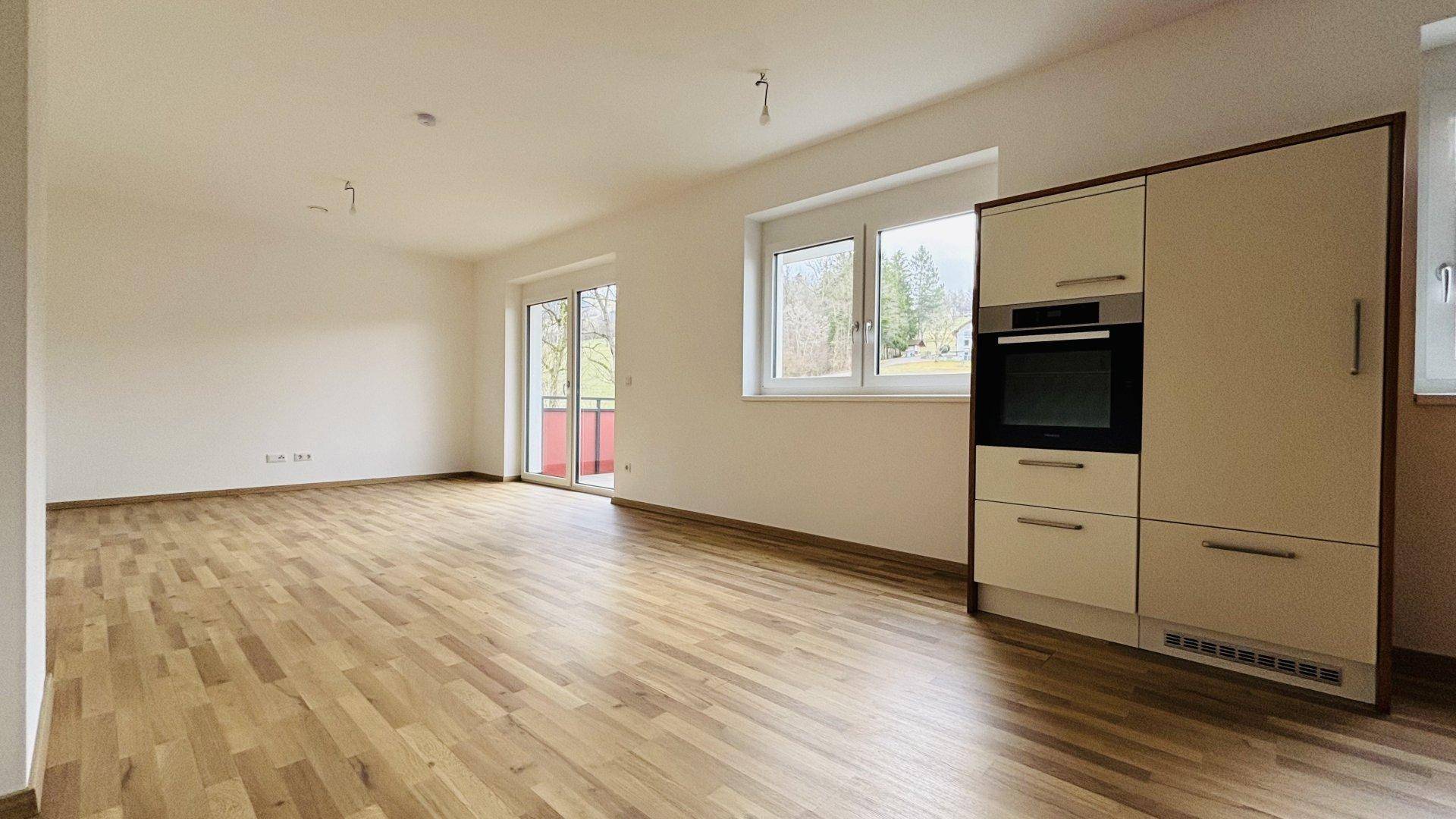 Geräumiger Wohnbereich mit Holzboden, integriertem Küchenschrank und Zugang zum Balkon.