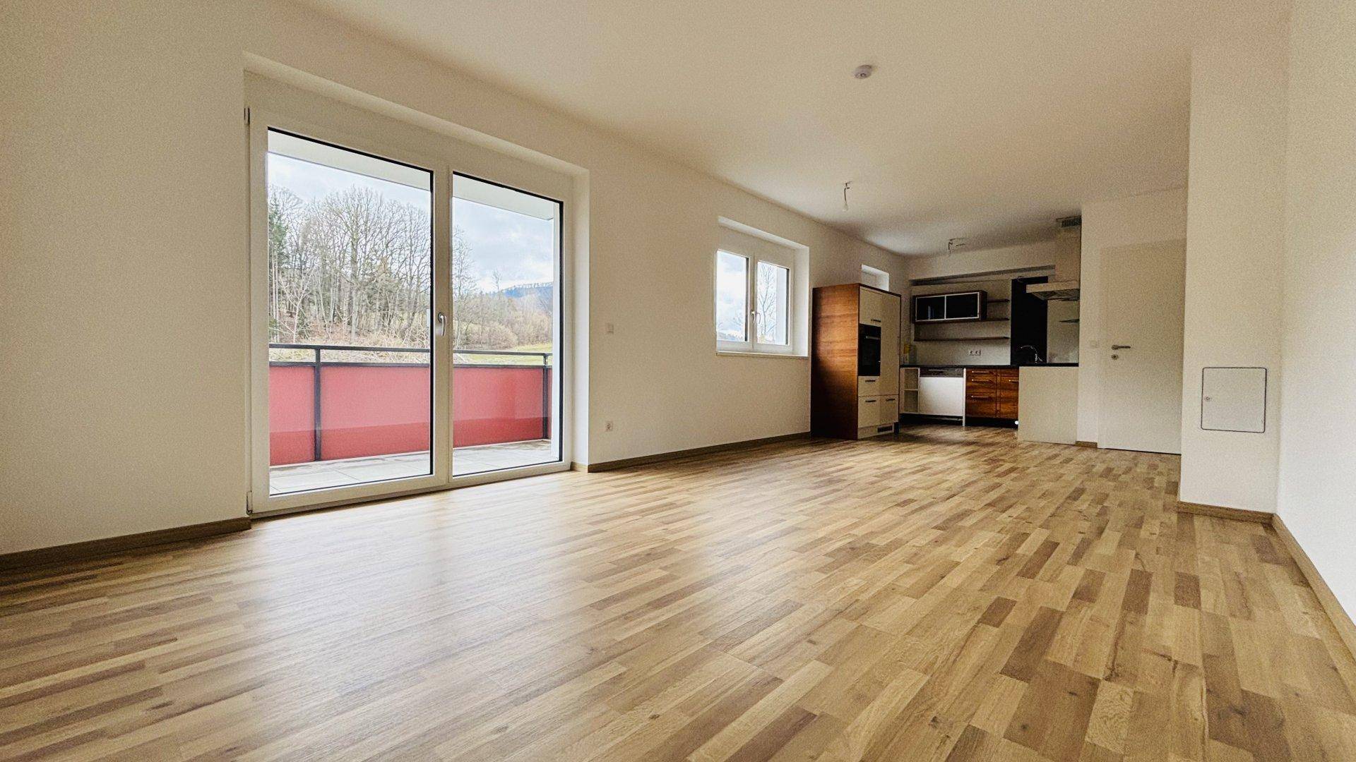 Offener Wohnbereich mit Holzboden, Blick auf die Küche und großem Balkonzugang.
