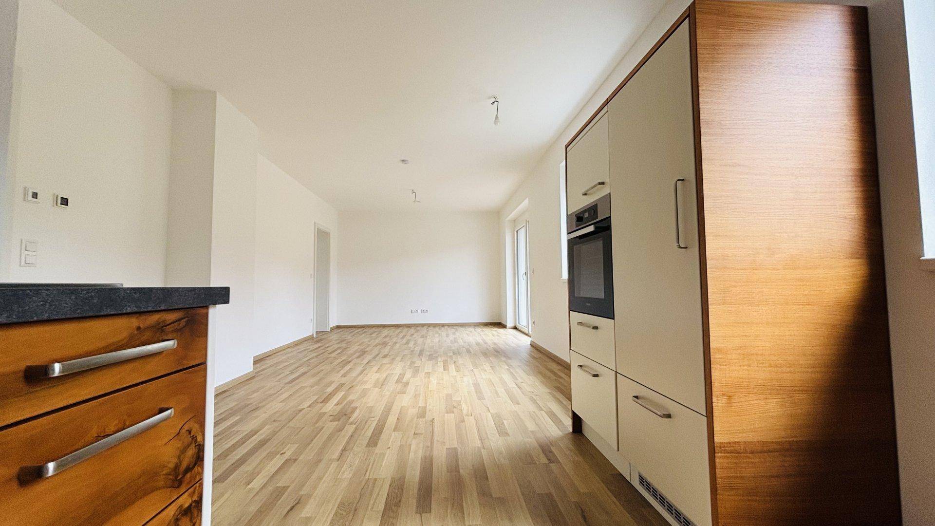 Heller offener Wohnbereich mit Holzboden und Blick auf die moderne Küchenzeile.