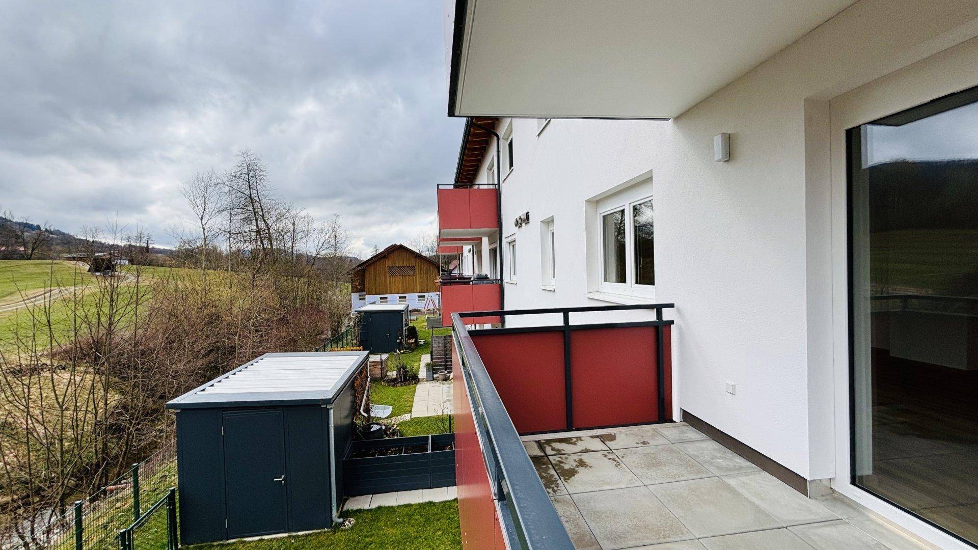 Balkon mit Fliesenboden und Blick auf die umliegende Natur und ein Gartenhaus.