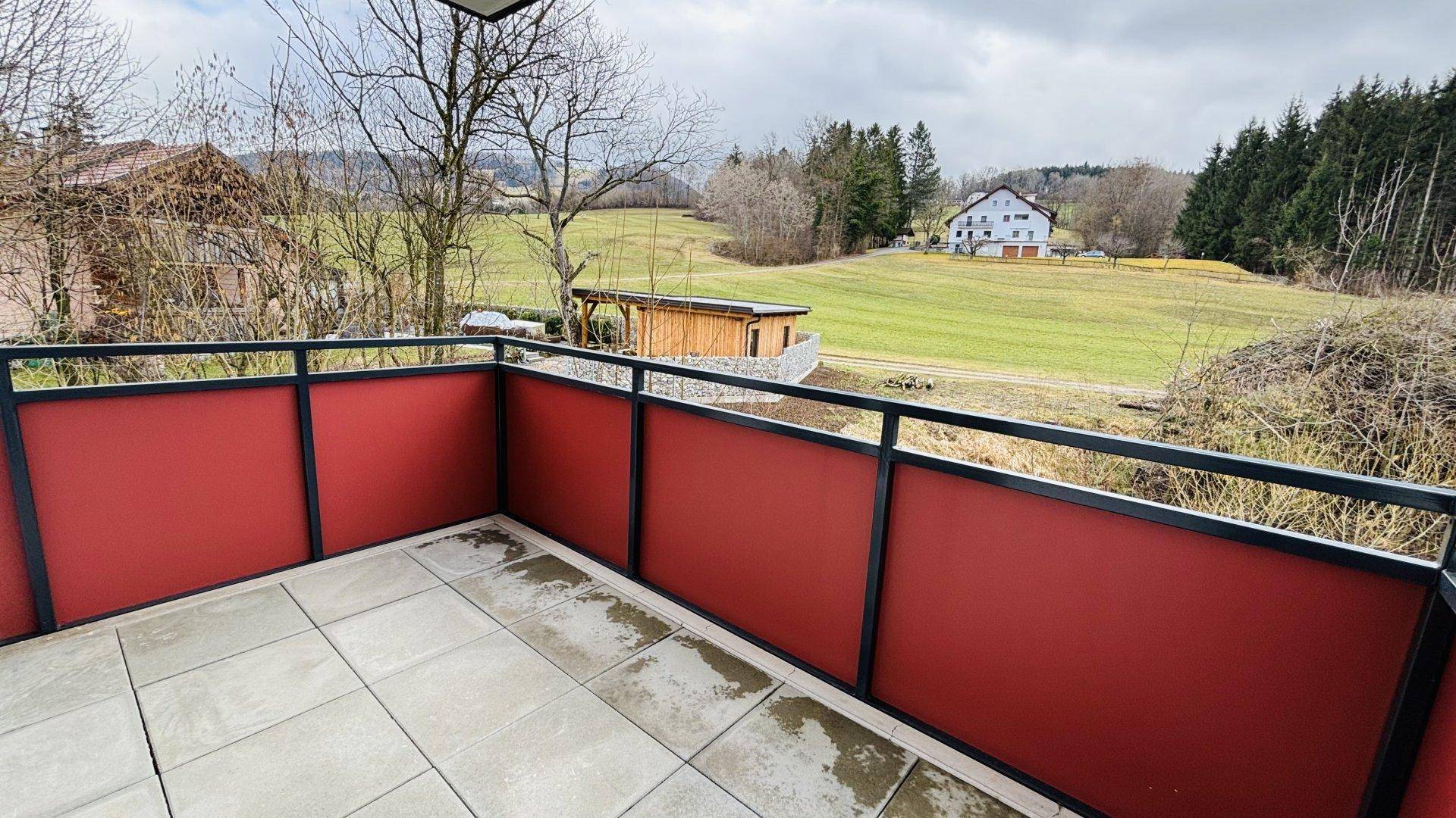 Geräumiger Balkon mit Fliesenboden und weitem Blick über die grüne Landschaft.