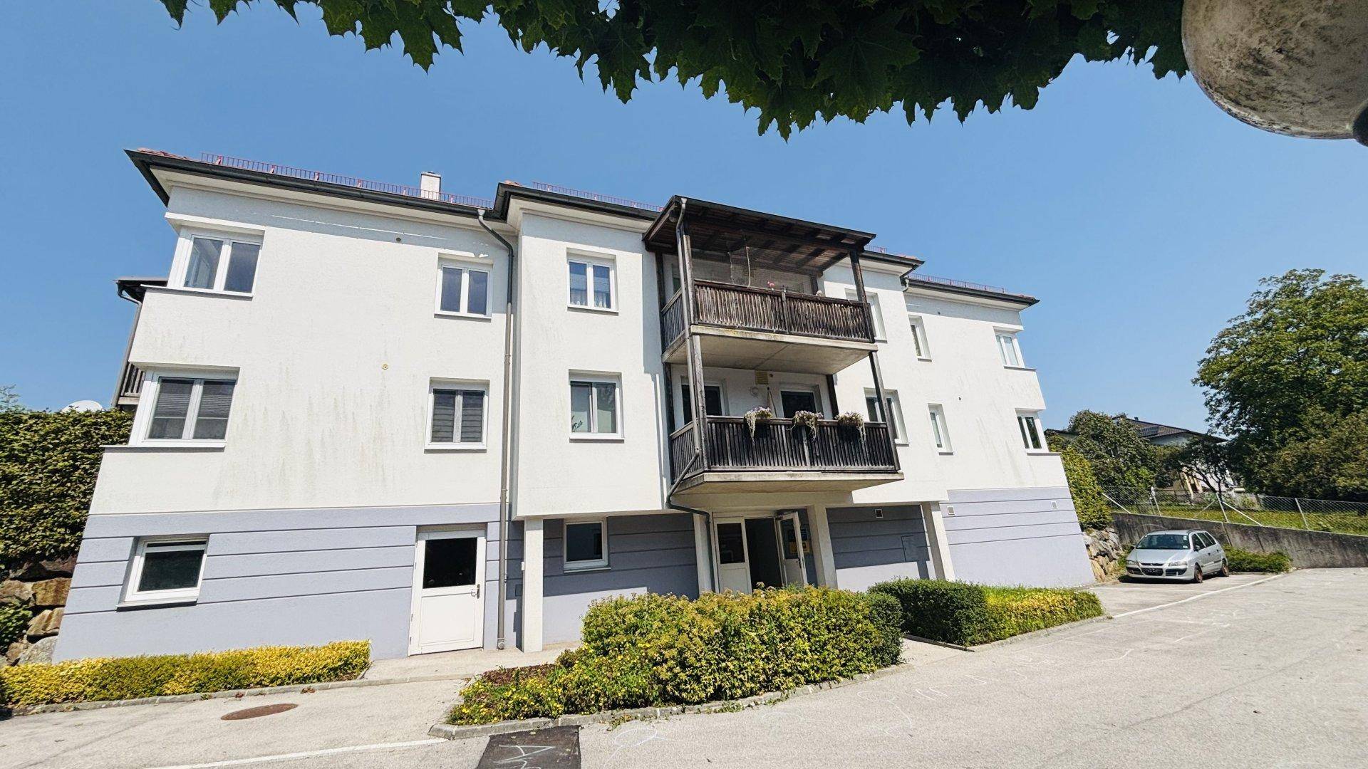 Ansicht des Mehrfamilienhauses mit Balkonen und Zufahrt, umgeben von gepflegten Sträuchern.