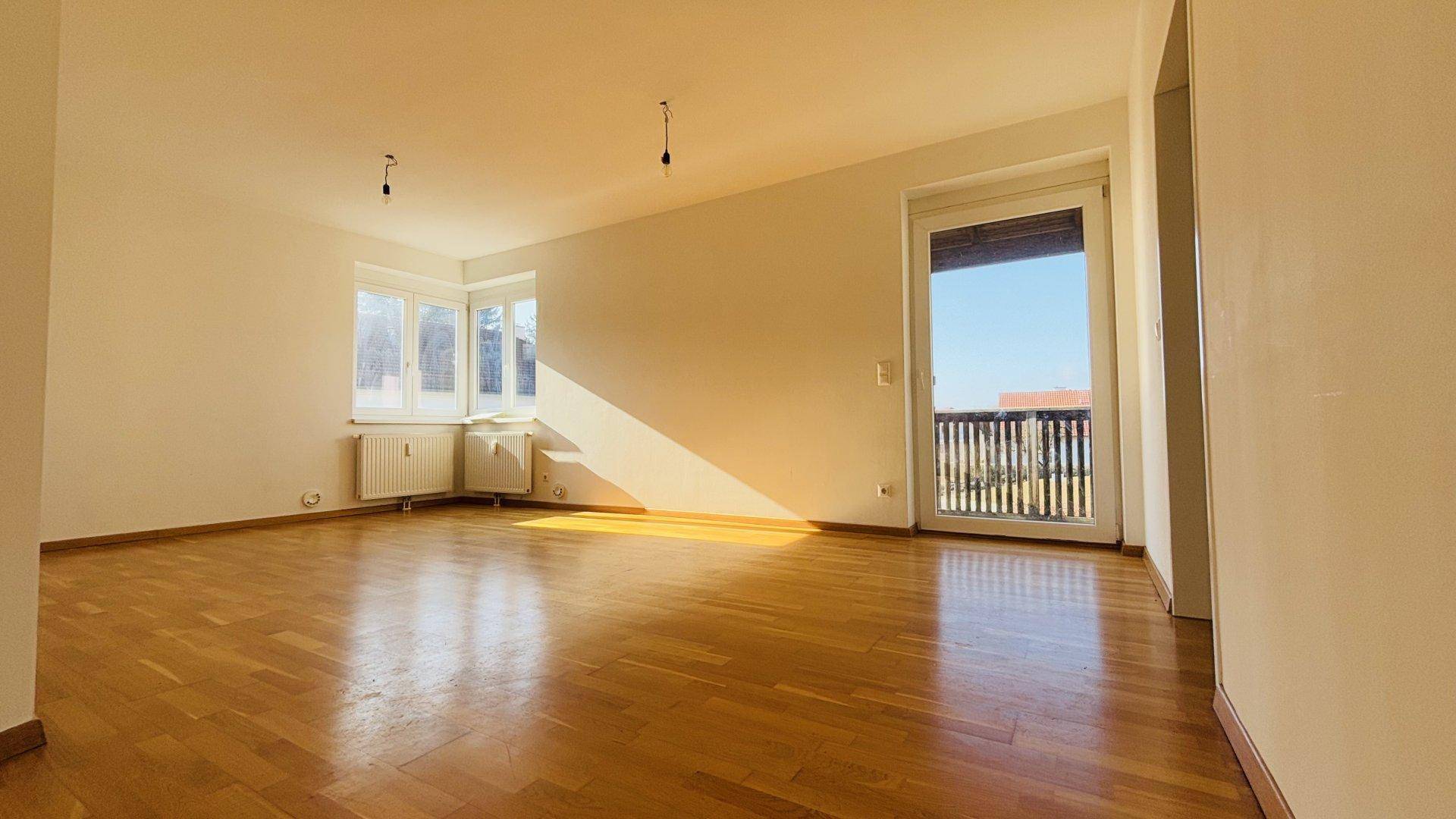 Geräumiges, helles Wohnzimmer mit Holzboden, Erkerfenster und Balkonzugang, sonnendurchflutet.