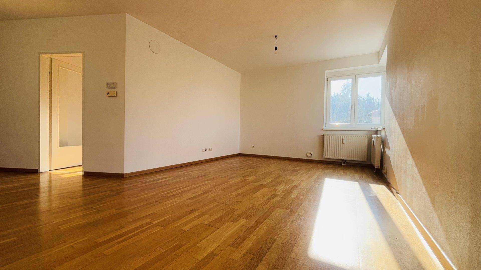 Großzügiger, heller Raum mit Holzboden und Fenster, ideal als Wohn- oder Schlafzimmer nutzbar.