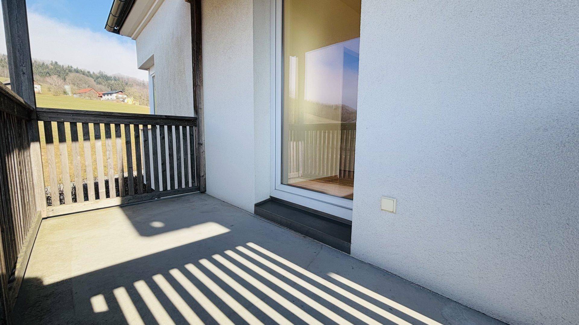 Heller Balkon mit Holzbalken und Zugang zum Innenbereich, sonnendurchflutet.