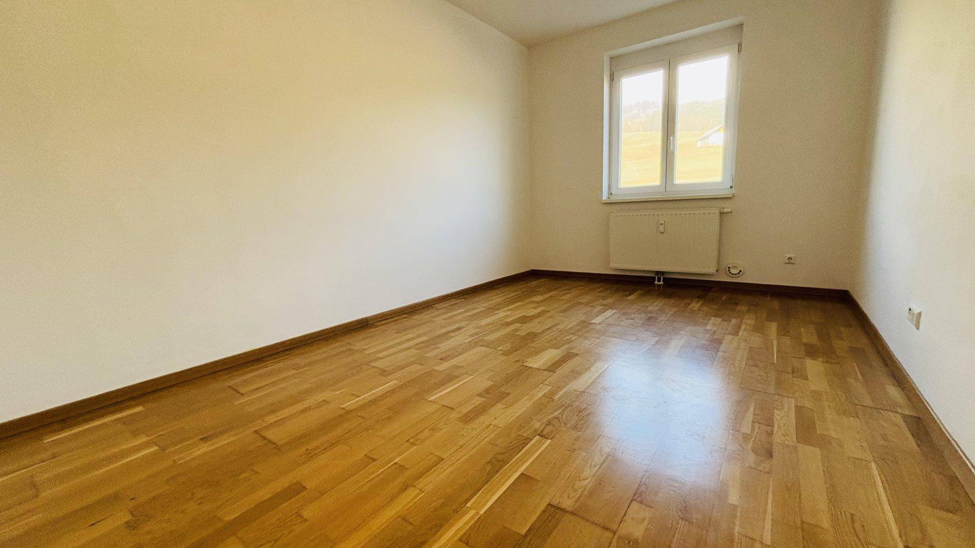 Helles Schlafzimmer mit Holzboden und Fenster, bereit zur individuellen Gestaltung.