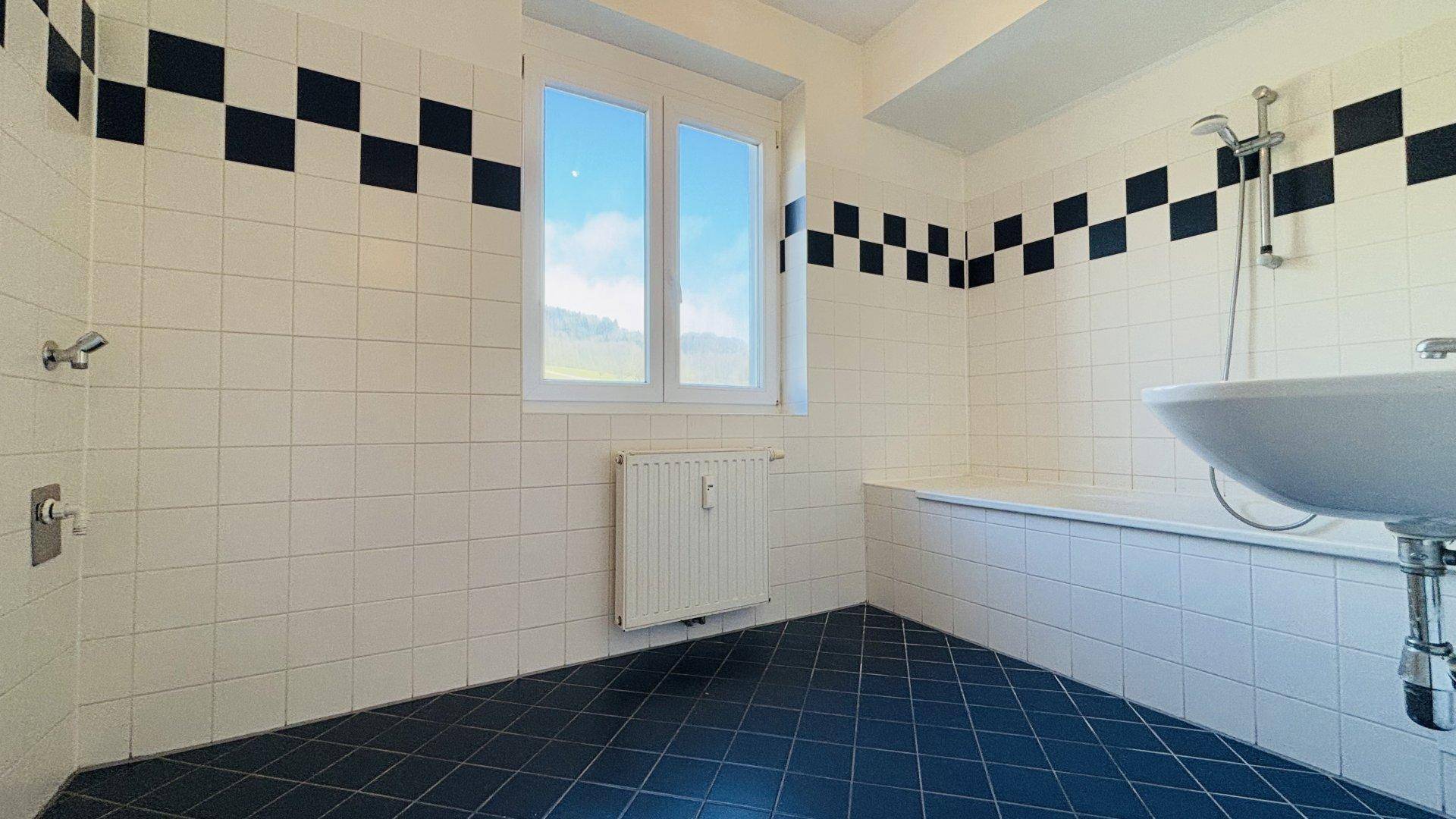 Badezimmer mit weißen und blauen Fliesen, Badewanne, Dusche und Fenster.