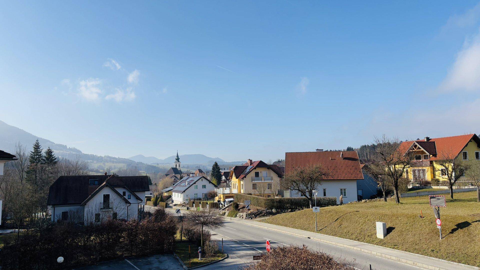 Panoramablick über eine ländliche Siedlung mit Häusern, Bergen und weitem Himmel.