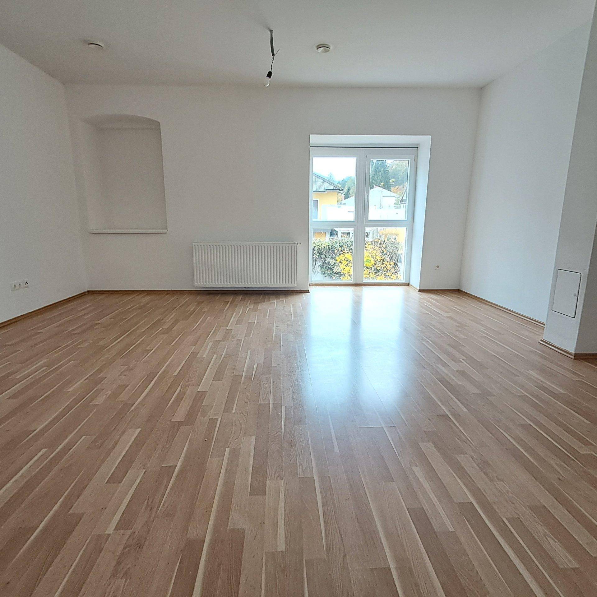 Heller, unmöblierter Raum mit Laminatboden und einer großen Fensterfront, die Zugang nach draußen bietet.