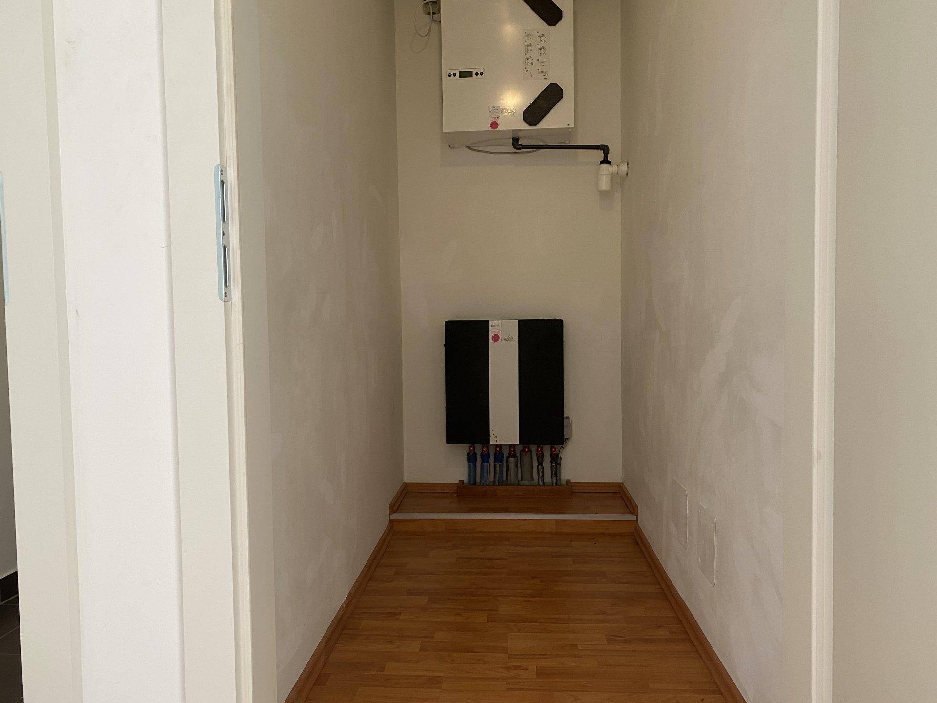 Kleiner Hauswirtschaftsraum mit technischen Installationen und Laminatboden, ideal für Haustechnik.