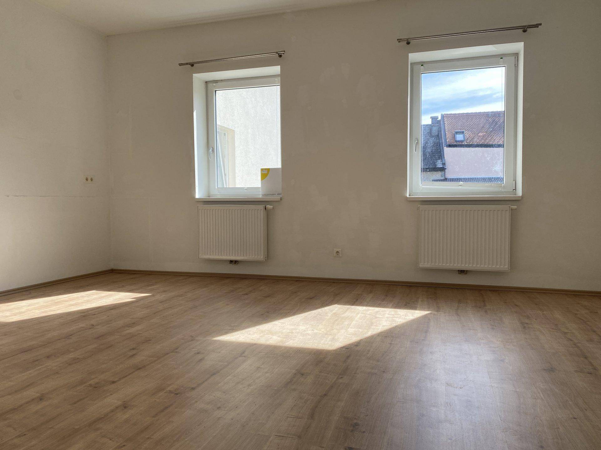 Geräumiger, leerer Raum mit zwei Fenstern und Laminatboden, der viel natürliches Licht empfängt.