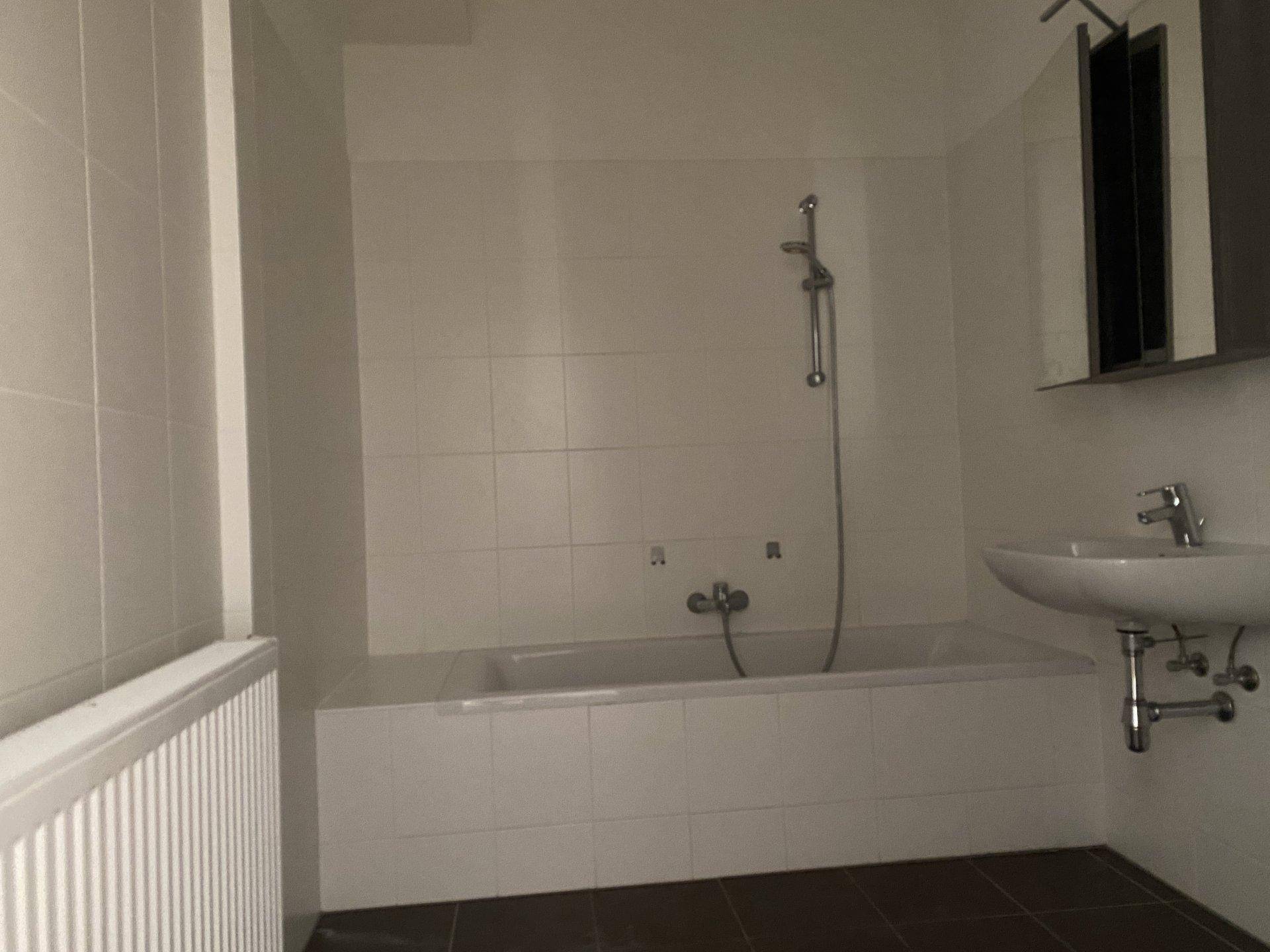 Badezimmer mit Badewanne, Waschbecken und weißen Fliesen, ausgestattet mit einem Heizkörper.