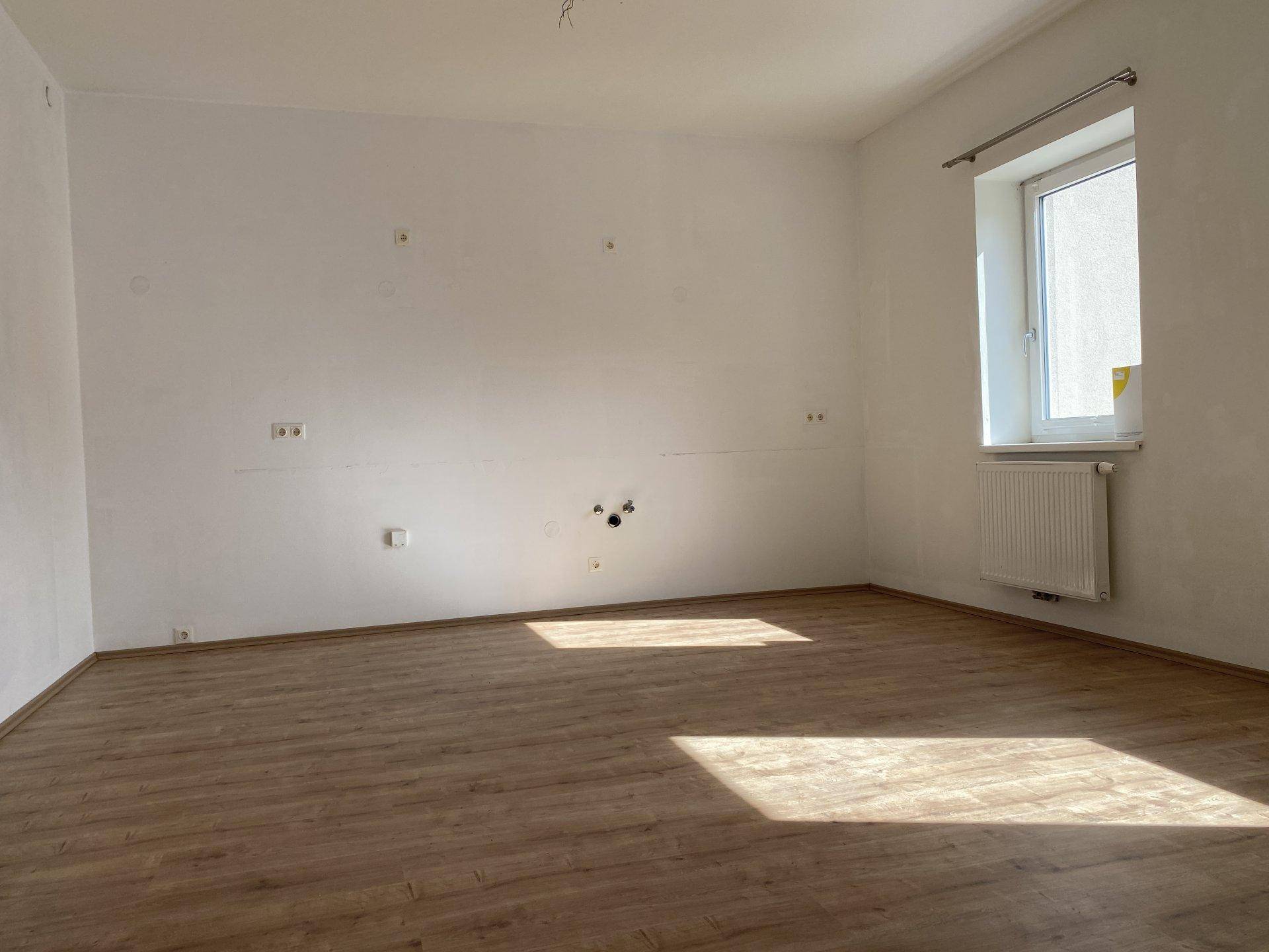 Heller, leerer Raum mit einem Fenster, Heizkörper und Laminatboden, ideal für individuelle Gestaltung.