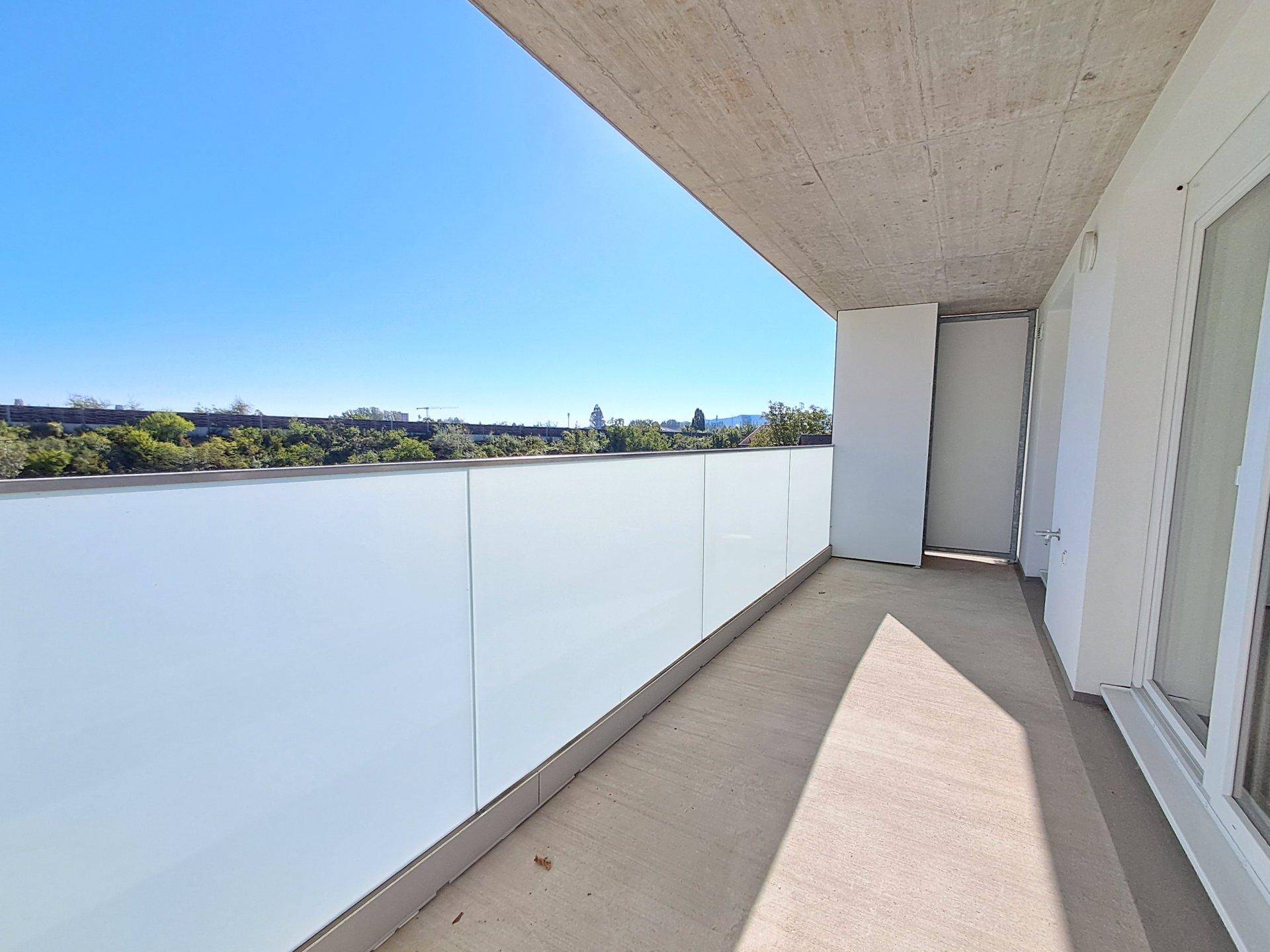 Heller Balkon mit moderner Glasbrüstung und weitem Blick ins Grüne.