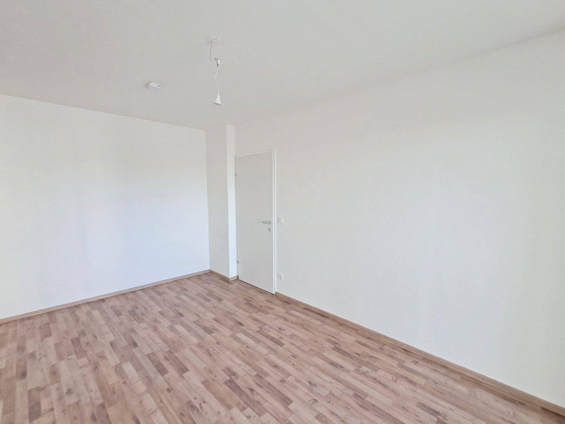 Helles Schlafzimmer mit Laminatboden und weiß gestrichenen Wänden.