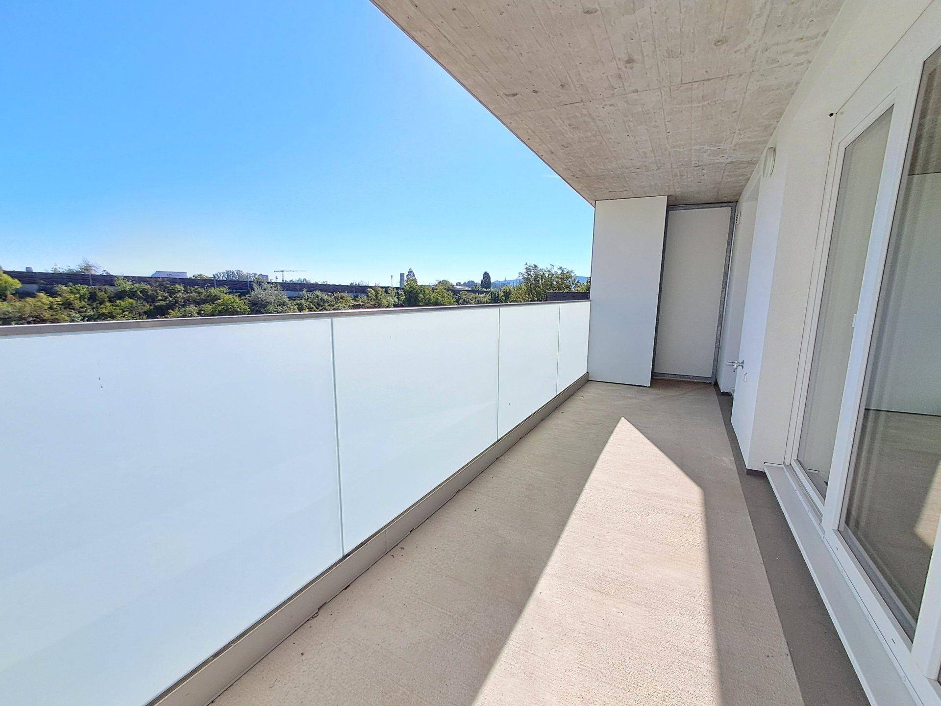 Heller Balkon mit moderner Glasbrüstung und Blick auf die grüne Umgebung.