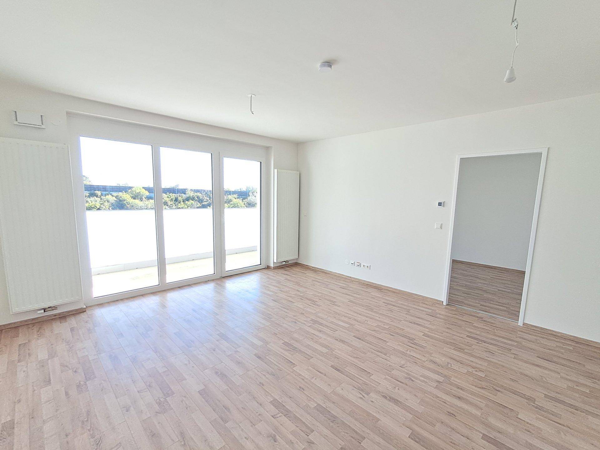 Helles Wohnzimmer mit großem Schiebefenster zum Balkon und Holzoptikboden.