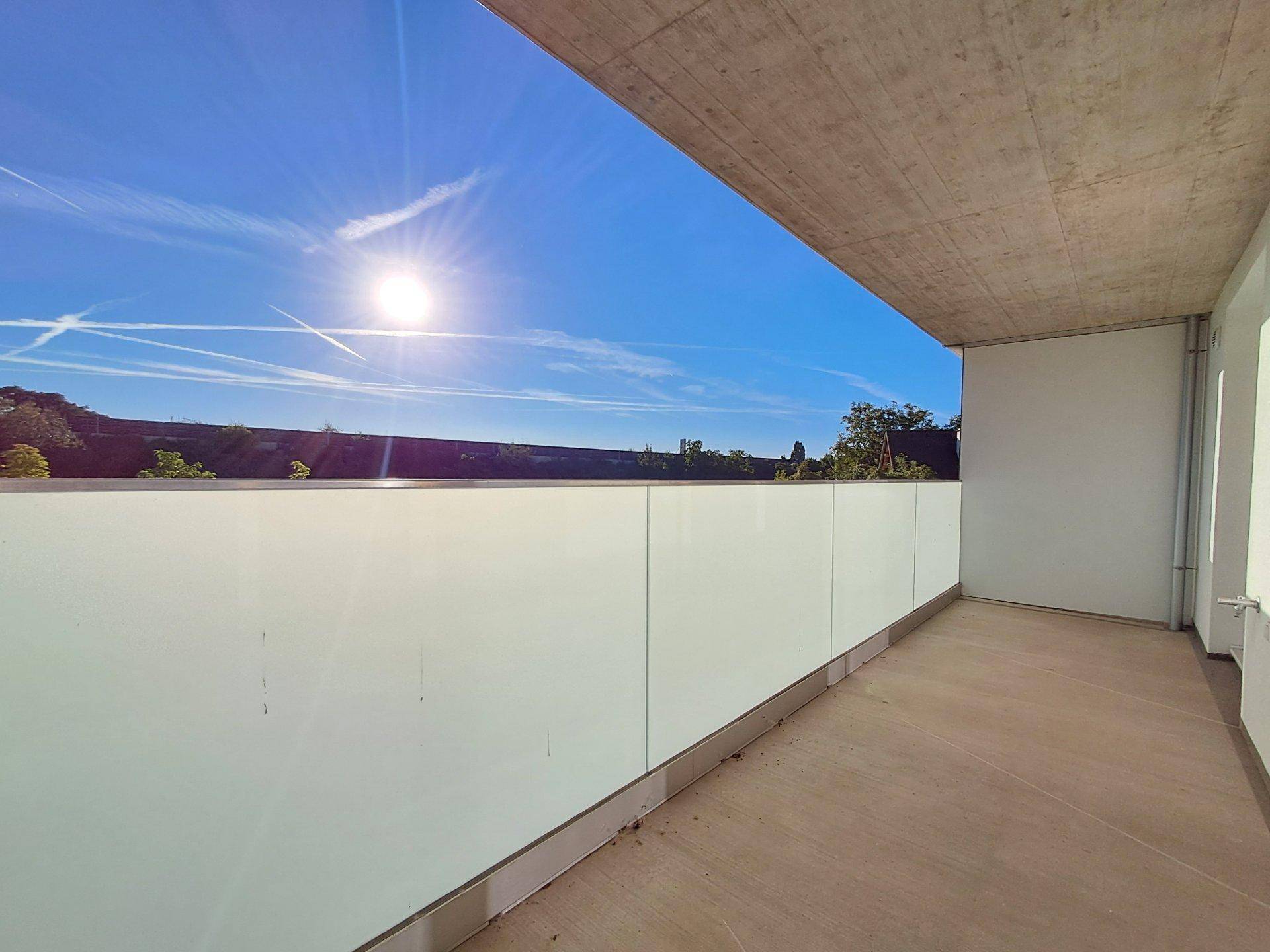Sonniger Balkon mit moderner Glasbrüstung und weitem Blick in die Ferne.