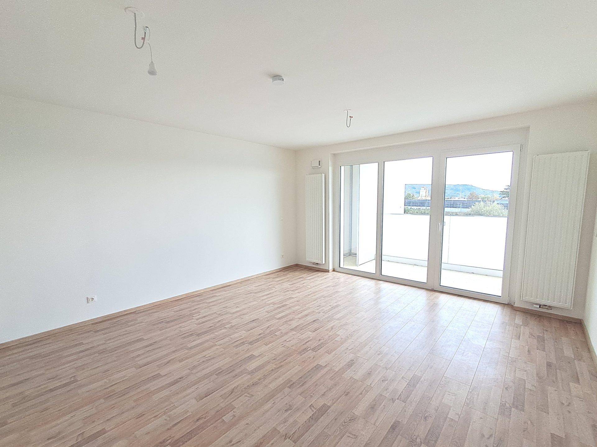 Helles Wohnzimmer mit Holzfußboden und großem Zugang zu einem Balkon.
