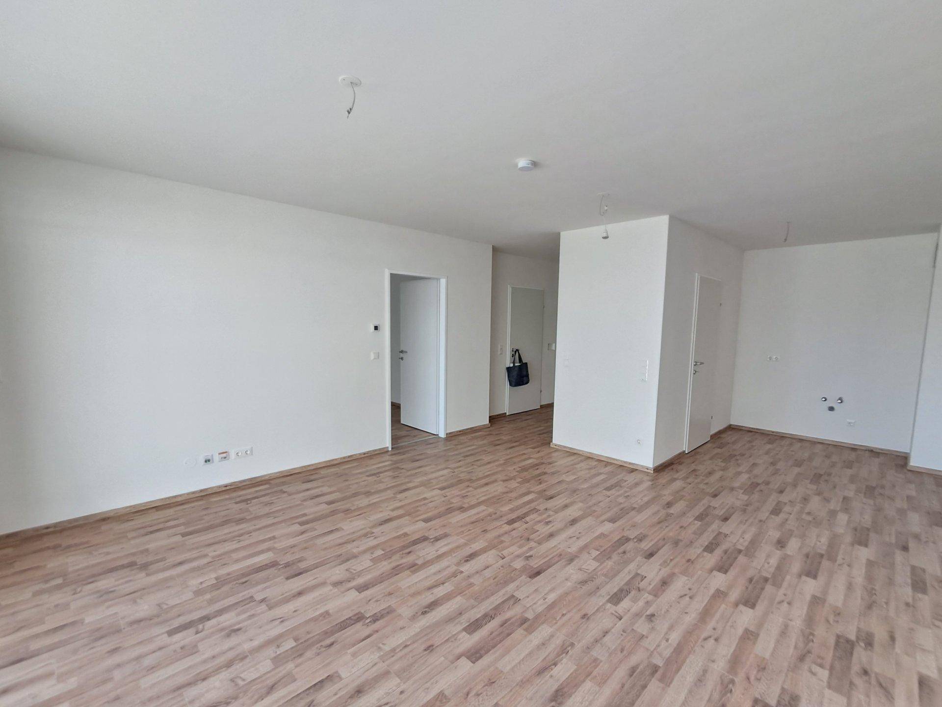 Leerer Wohnbereich mit hellem Laminatboden und weißen Wänden, bereit zur Einrichtung.