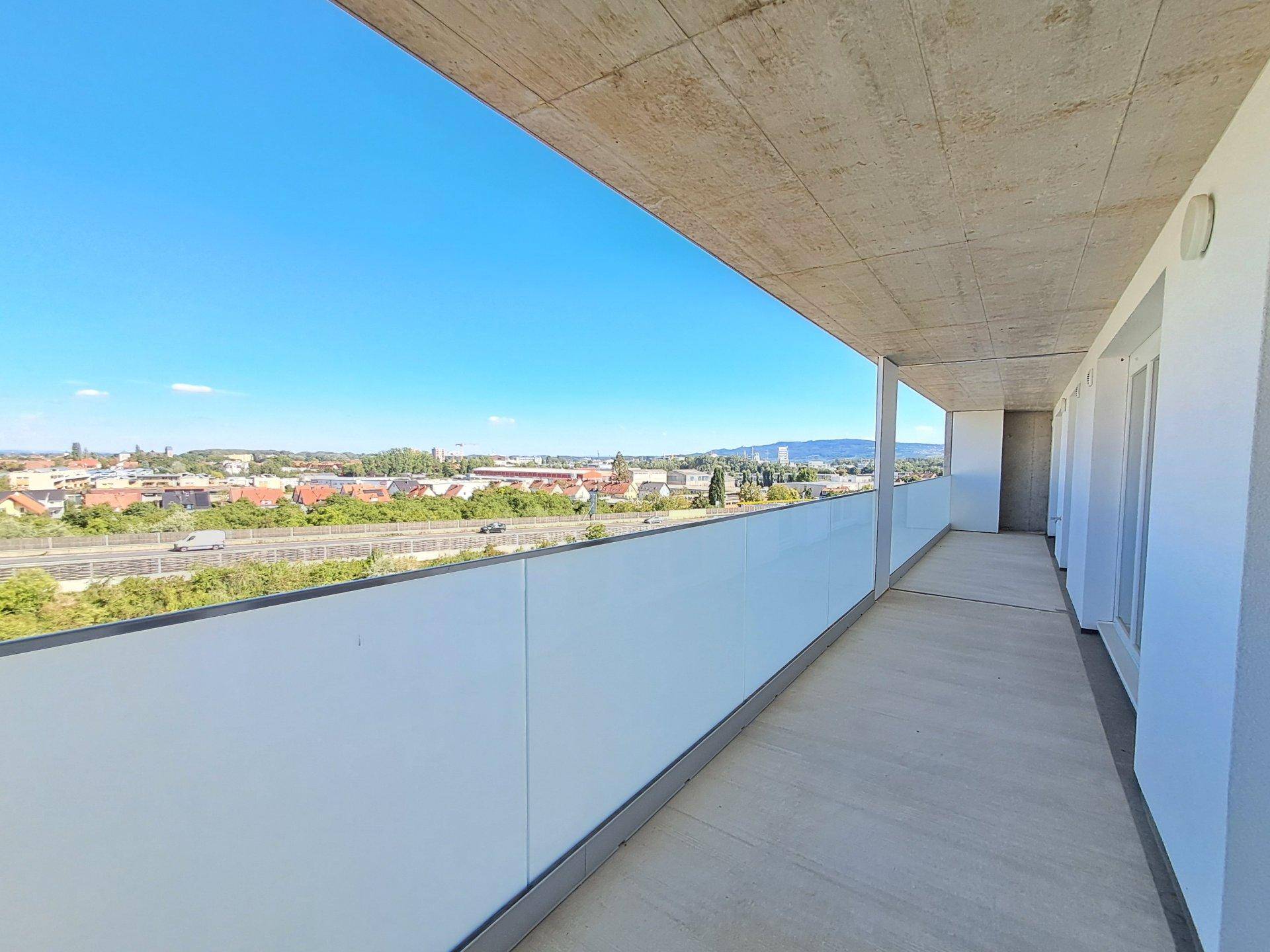 Langer Balkon mit Glasbrüstung und weitem Blick über die Stadt und die Umgebung.