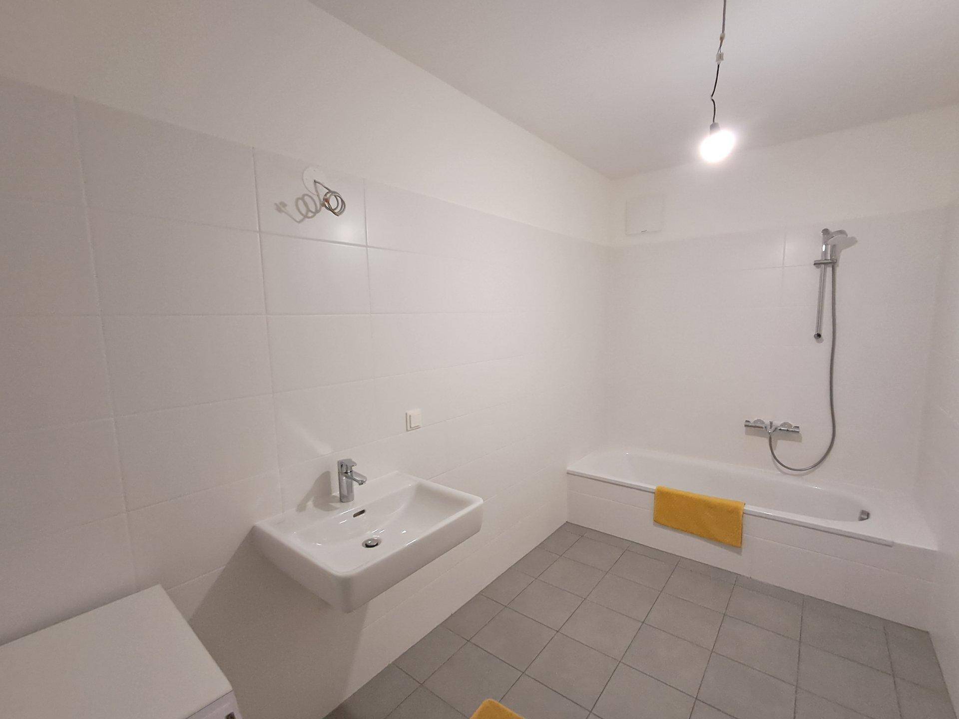 Modernes Badezimmer mit Badewanne, Waschbecken und weißen Fliesen an Wänden und Boden.