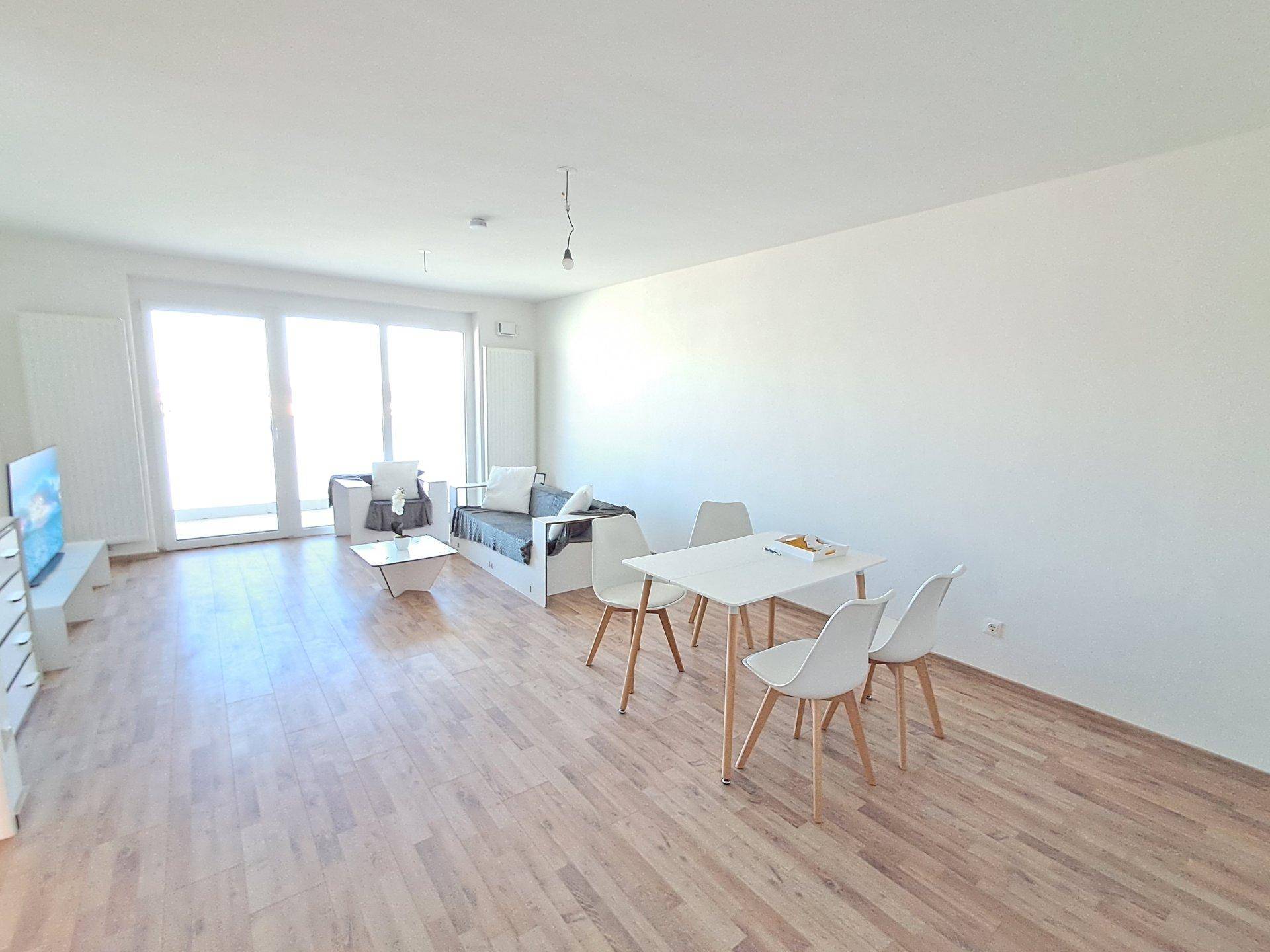 Lichtdurchfluteter Wohn- und Essbereich mit Zugang zum Balkon und hellem Laminatboden.