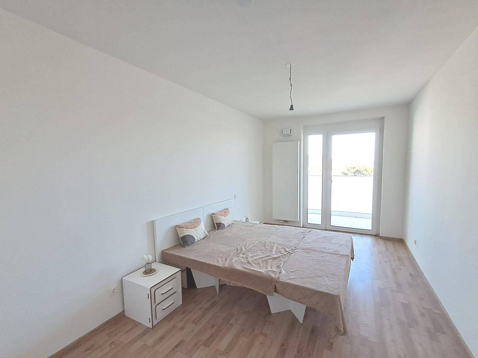 Schlafzimmer mit Zugang zum Balkon, hellem Laminatboden und viel natürlichem Licht.