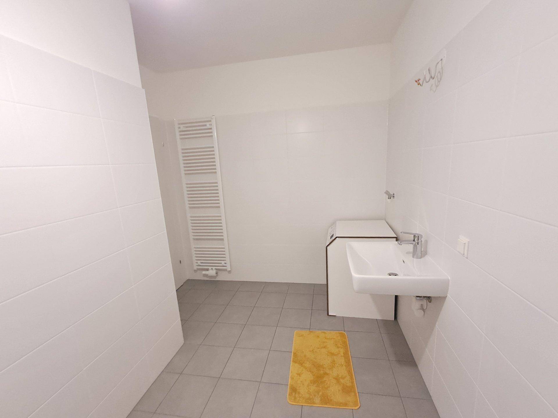 Helles Badezimmer mit Waschbecken, Handtuchheizkörper und Platz für eine Waschmaschine.
